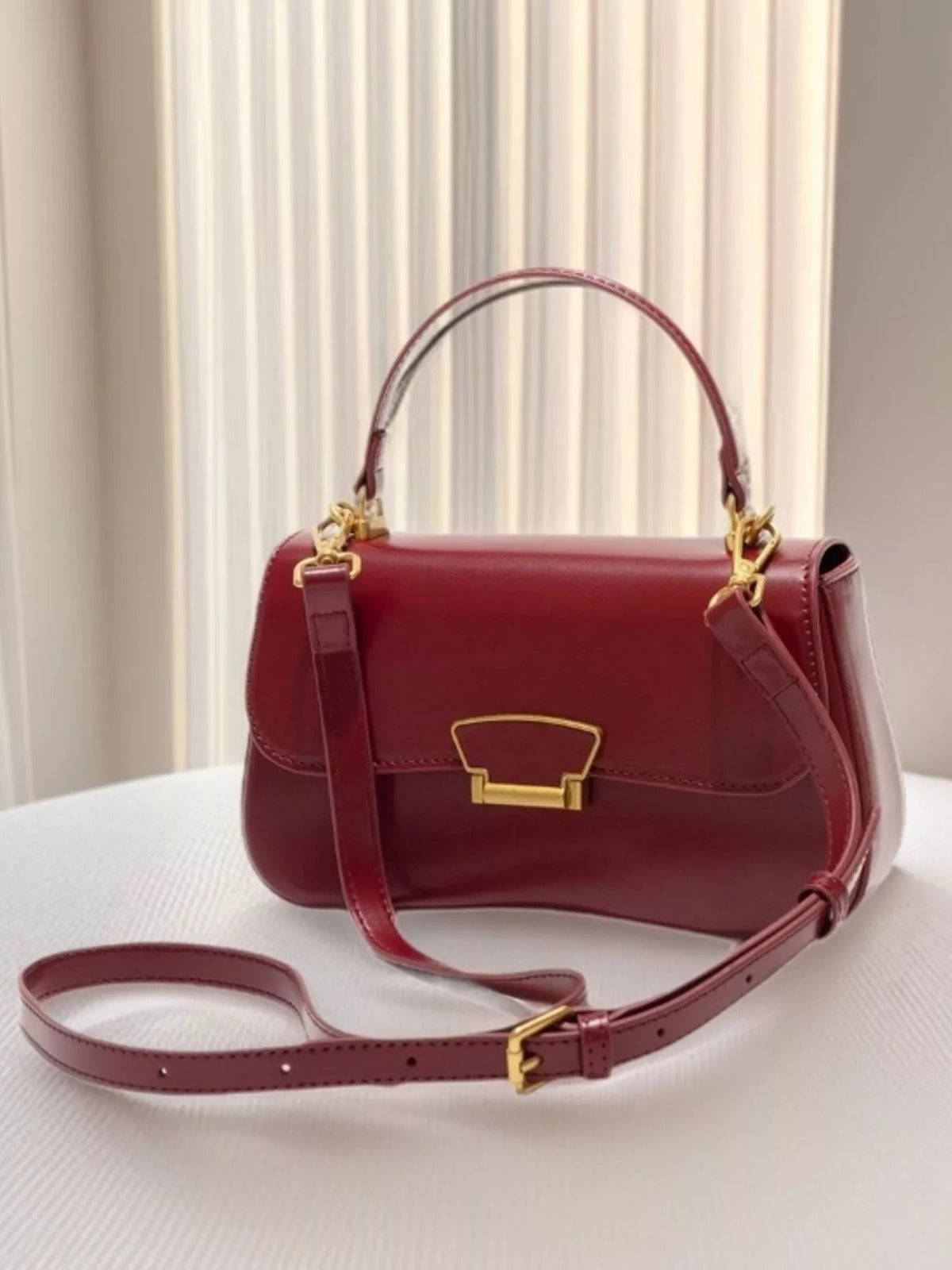 Small burgundy PU leather crossbody bag with a structured rectangular silhouette, top handle, adjustable strap, stitched flap, and gold-tone clasp.