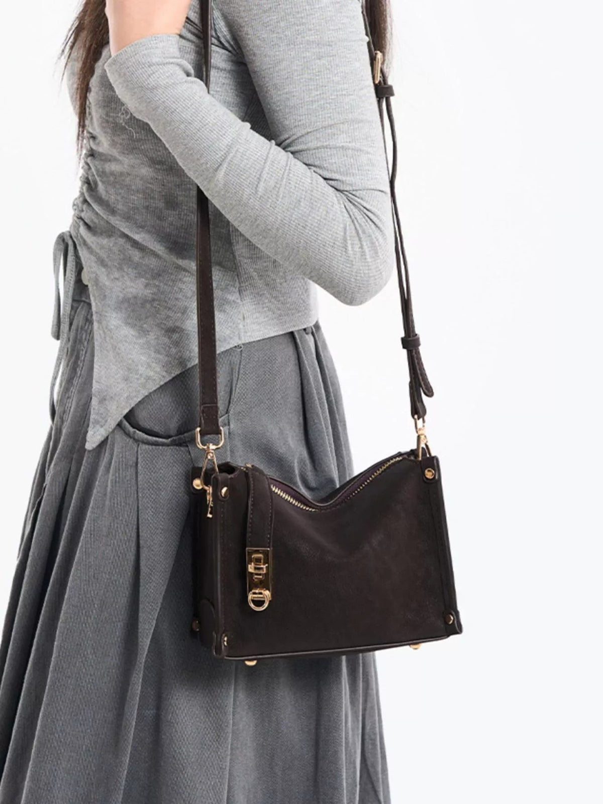 A model poses with a small black PU leather crossbody bag featuring an adjustable strap, zip-top construction, gold-tone hardware, and a structured silhouette.