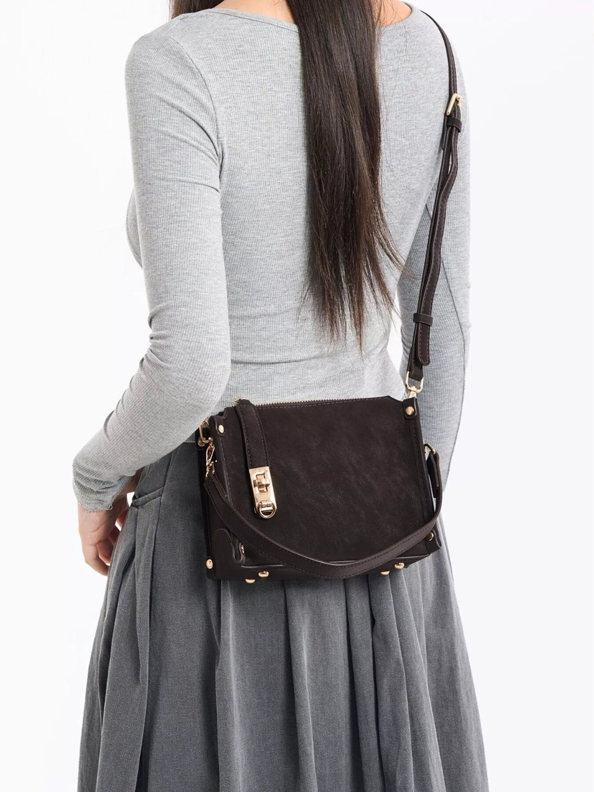 A model shown from behind wears a small black PU leather crossbody bag with an adjustable strap, structured rectangular silhouette, flap closure, and gold-tone hardware.