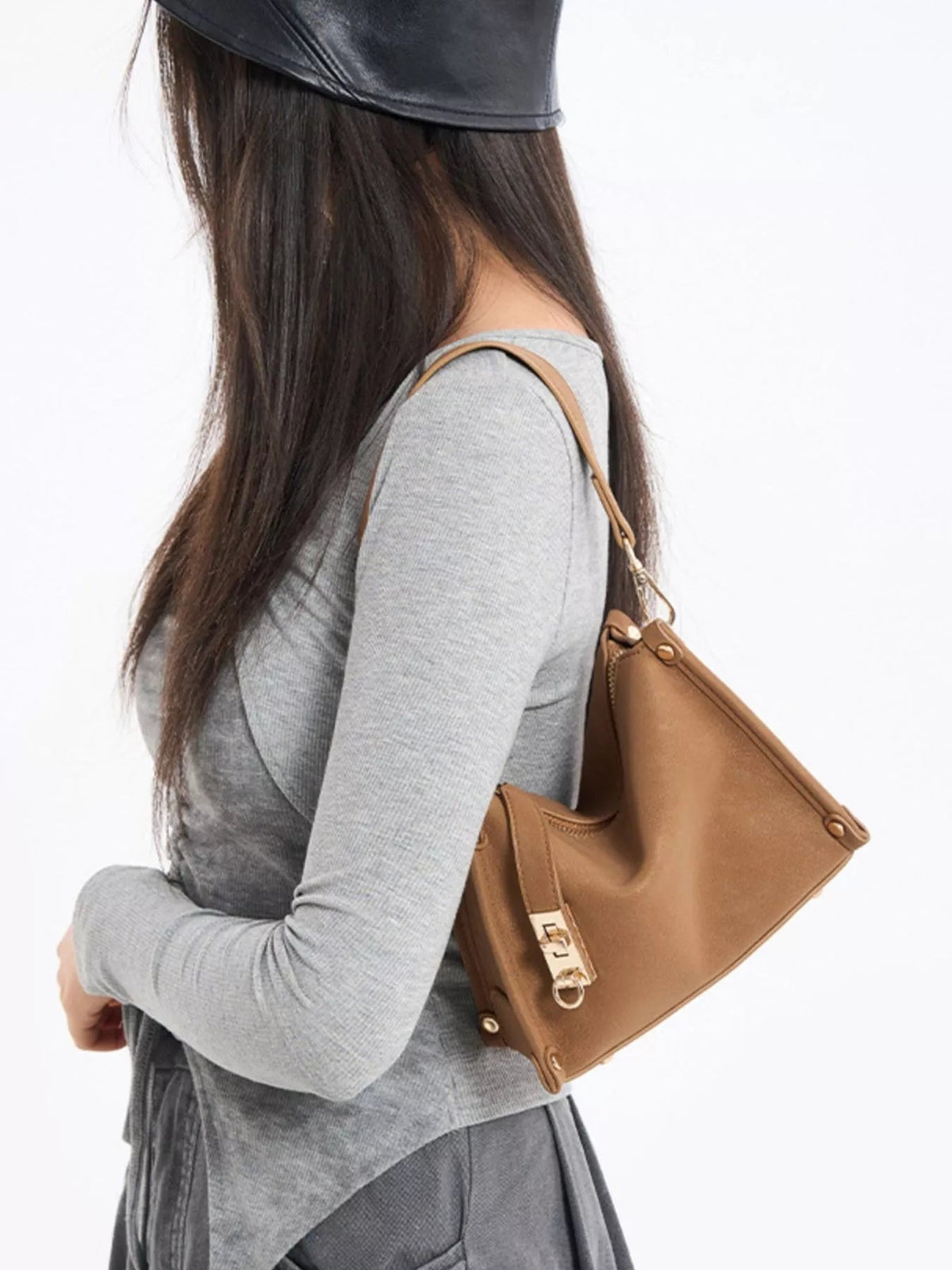 A model poses in profile with a small tan PU leather crossbody bag featuring an adjustable strap, structured silhouette, and gold-tone hardware.