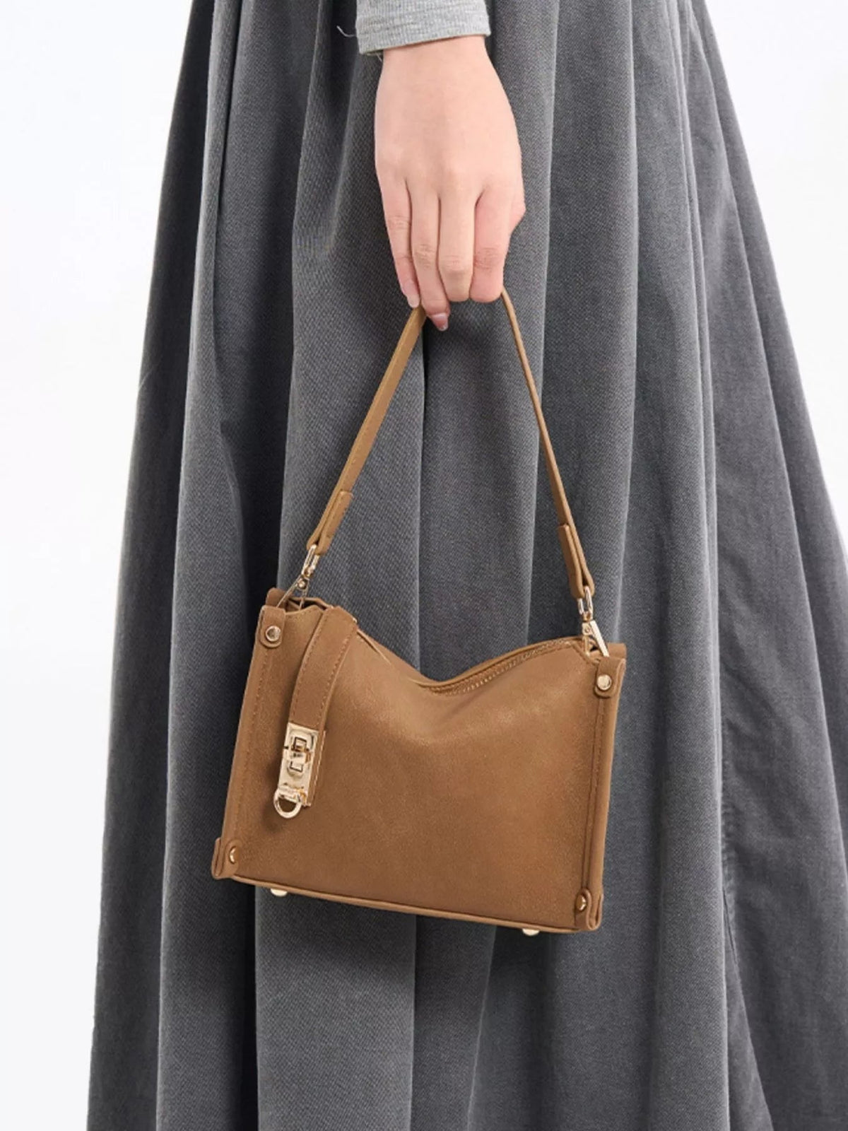 A model holds a small brown PU leather crossbody bag with an adjustable strap, zip-top closure, structured silhouette, and front clasp detail.