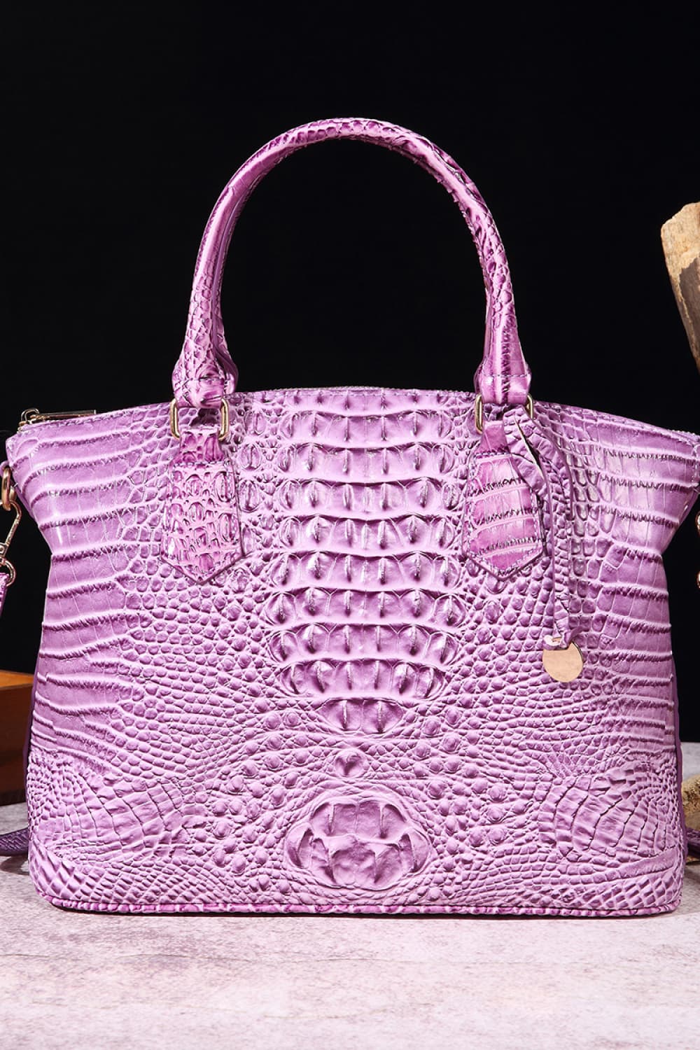 Medium purple PU leather handbag with a structured silhouette, rounded top handles, zip-top opening, and bold raised embossed texture.