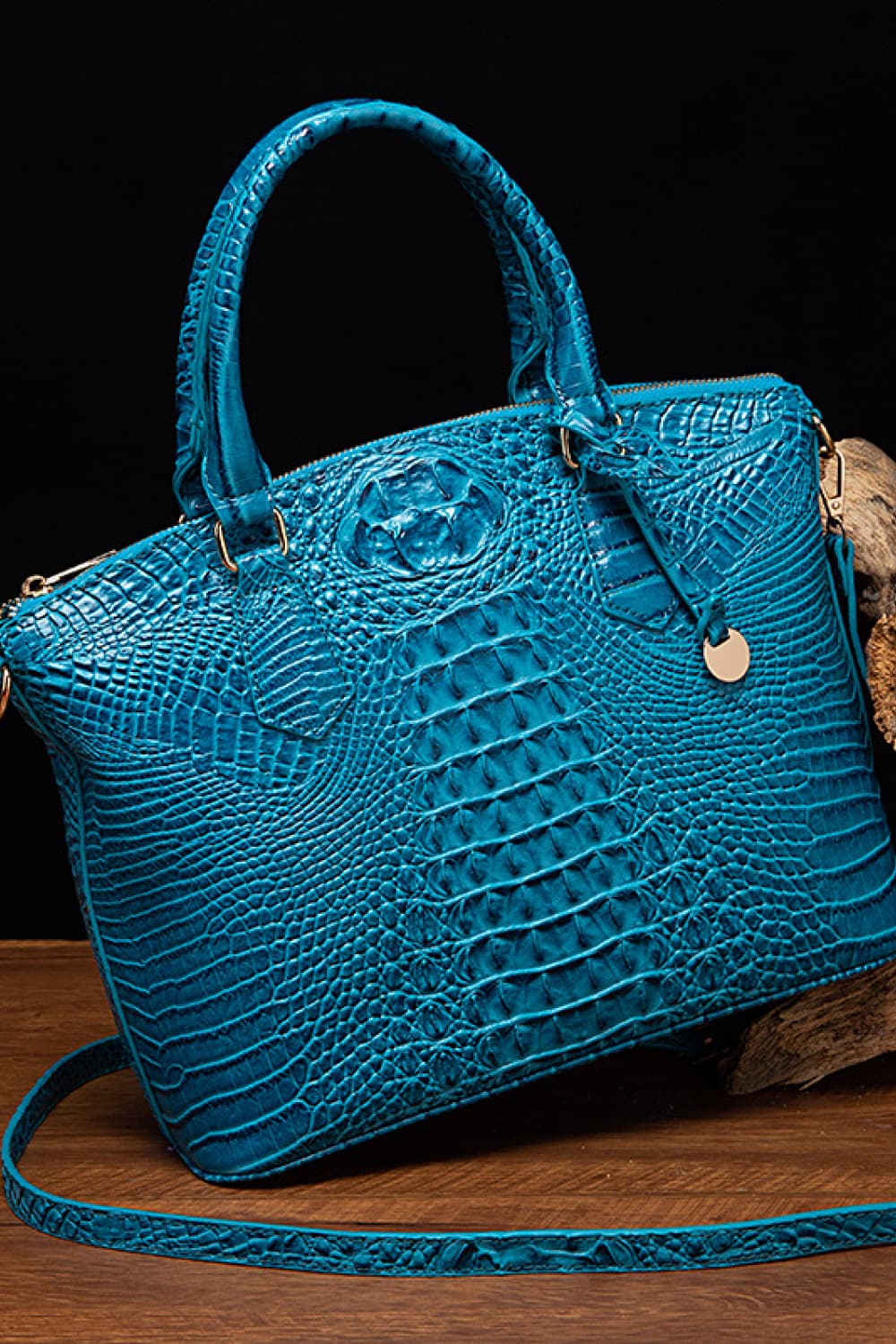 Medium blue PU leather handbag with a structured silhouette, rounded top handles, crocodile-inspired embossed texture, removable shoulder strap, and hanging charm.