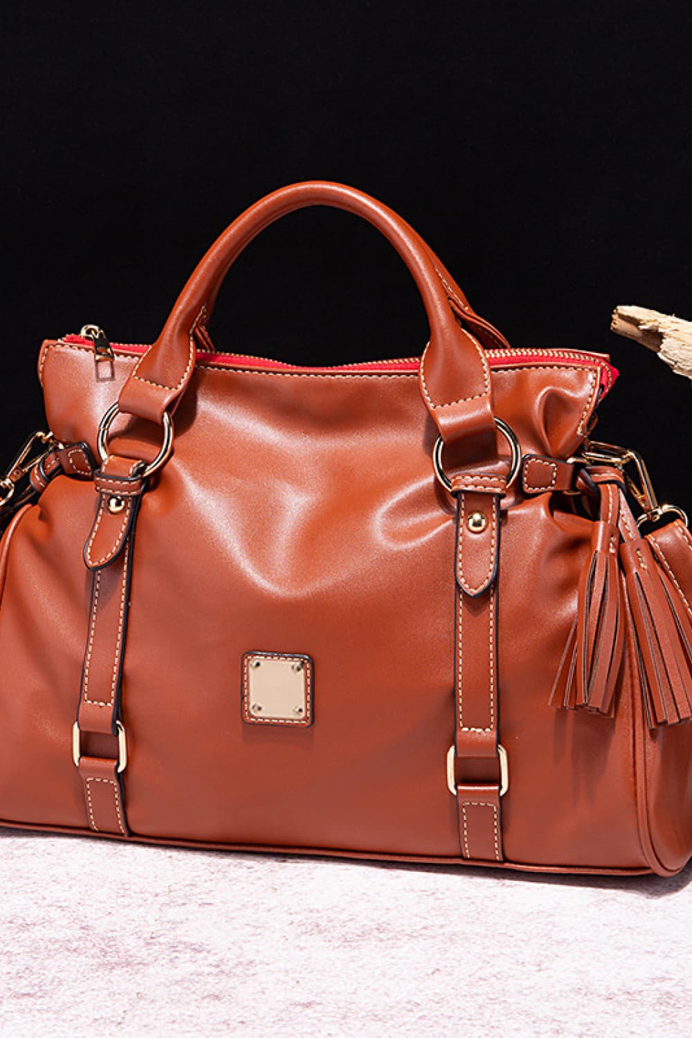 Large brown PU leather handbag with a spacious structured silhouette, rounded top handles, top zip closure, adjustable strap details, gleaming hardware, and tassel accents.