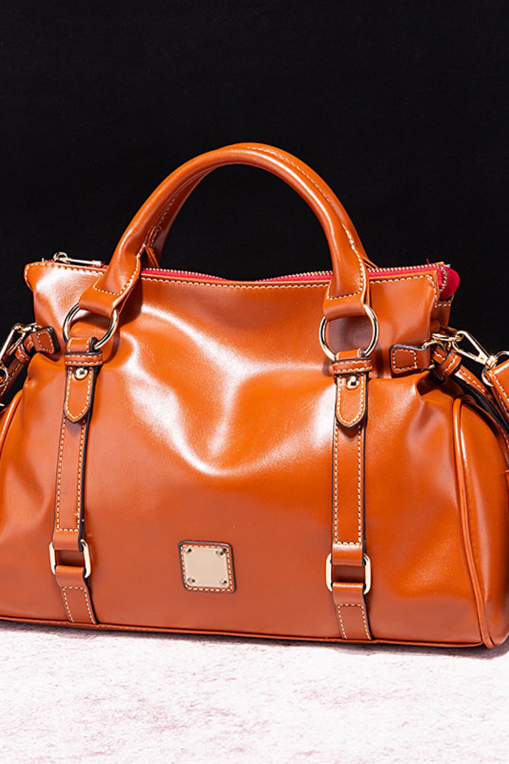 Large orange-brown PU leather handbag with rounded top handles, a zip closure, structured silhouette, adjustable side straps, and gleaming metal hardware.