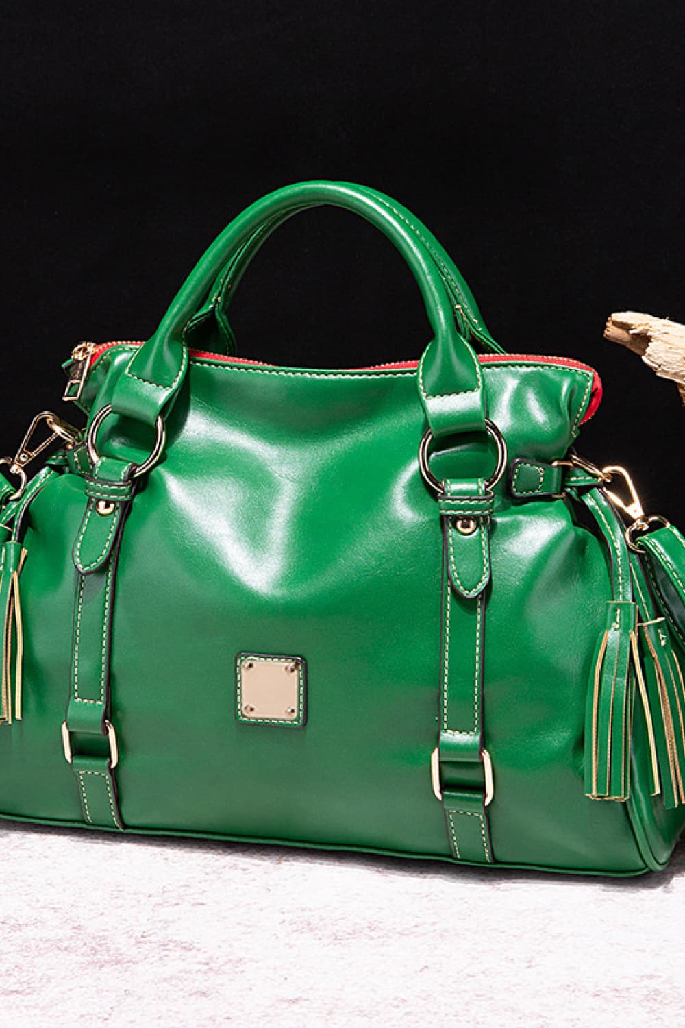 Large green PU leather handbag with a structured silhouette, rounded top handles, top zip closure, adjustable strap details, gold hardware, and tassel accents.