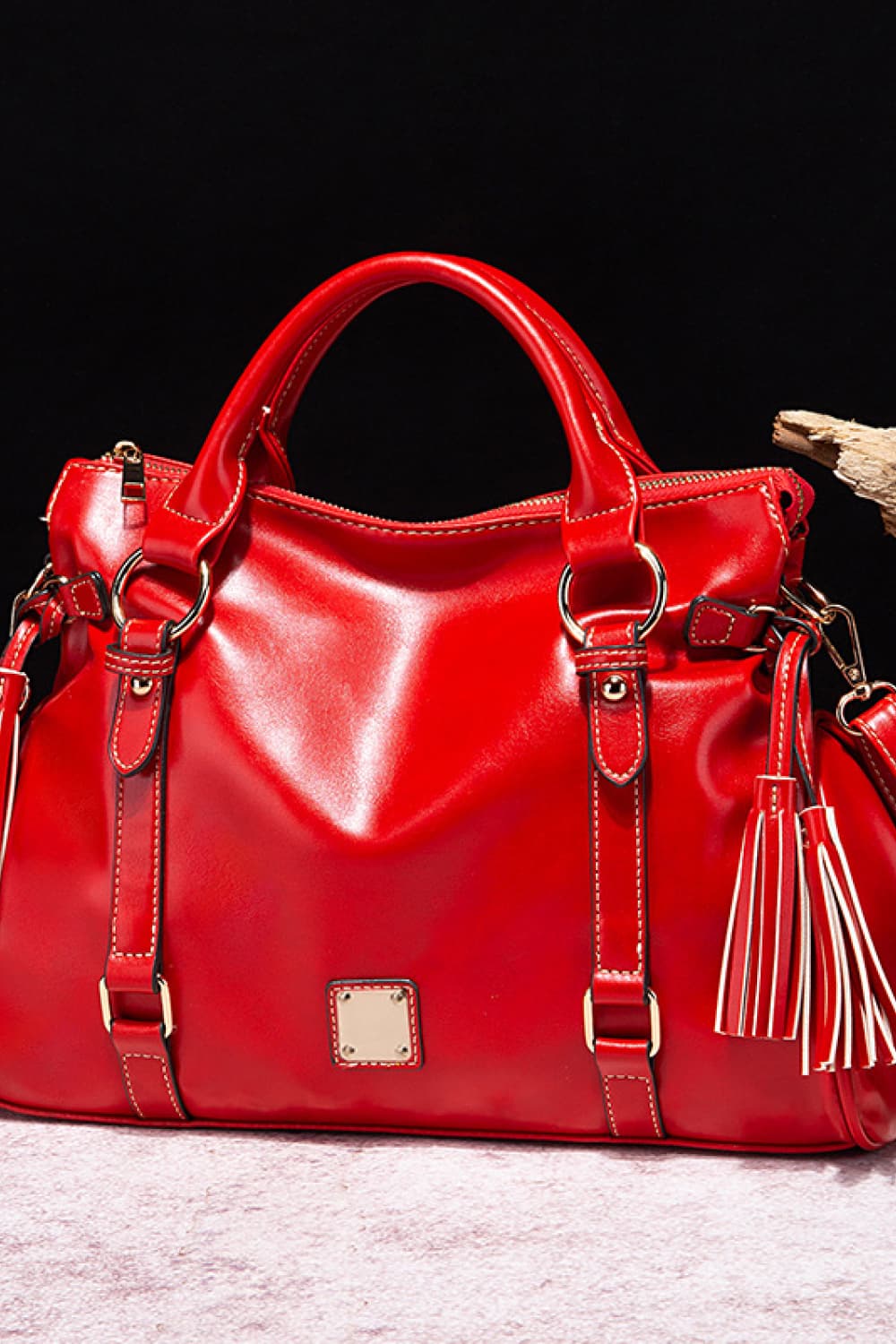 Large red PU leather handbag with rounded top handles, a softly structured silhouette, metal hardware, stitched straps, and long tassel accents.
