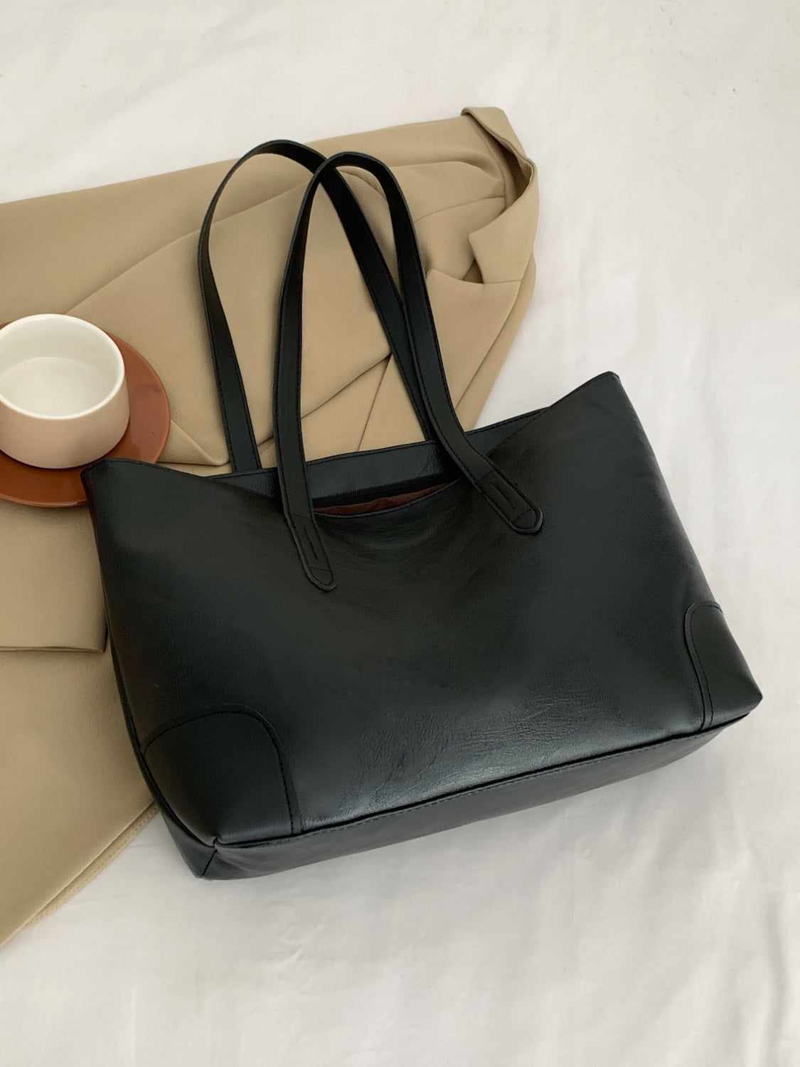 Black PU leather medium tote bag with a softly structured silhouette, long shoulder straps, open top, clean paneling, and reinforced corner details.