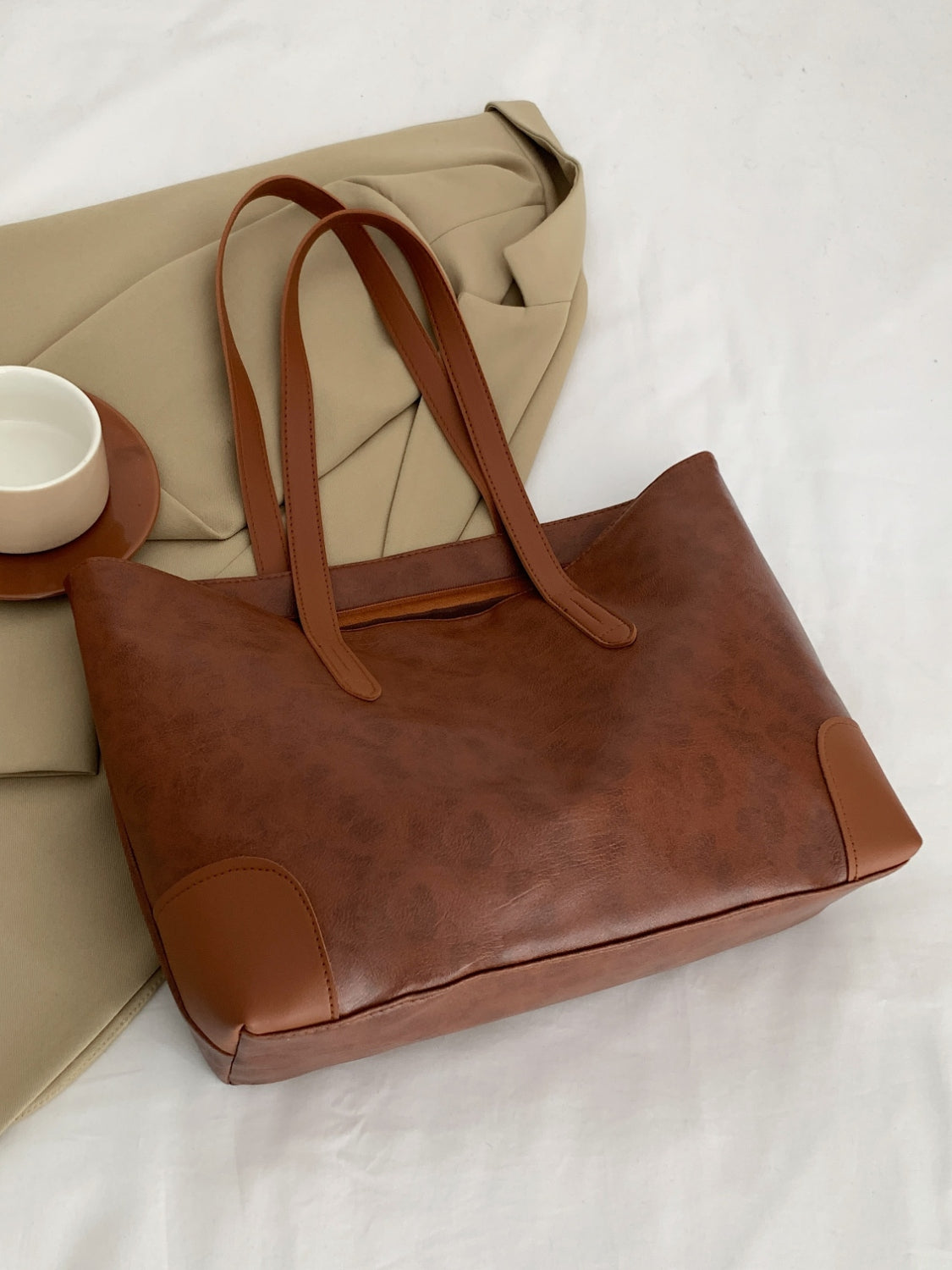 Brown PU leather medium tote bag with a softly structured silhouette, long shoulder straps, clean paneling, neat topstitching, and reinforced corner details.