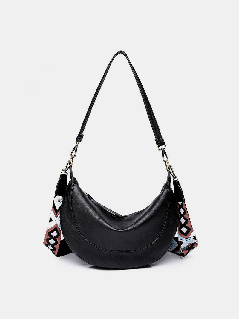 Large black PU leather crossbody bag with a softly curved crescent silhouette, smooth rounded front, and removable patterned strap with metal clip hardware.