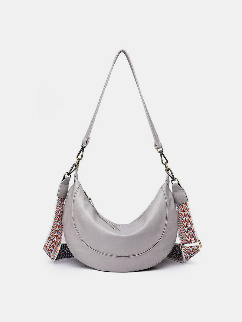 Large gray PU leather crossbody bag with a softly curved crescent silhouette, gathered sides, secure zip top, and a removable strap with metal clips.