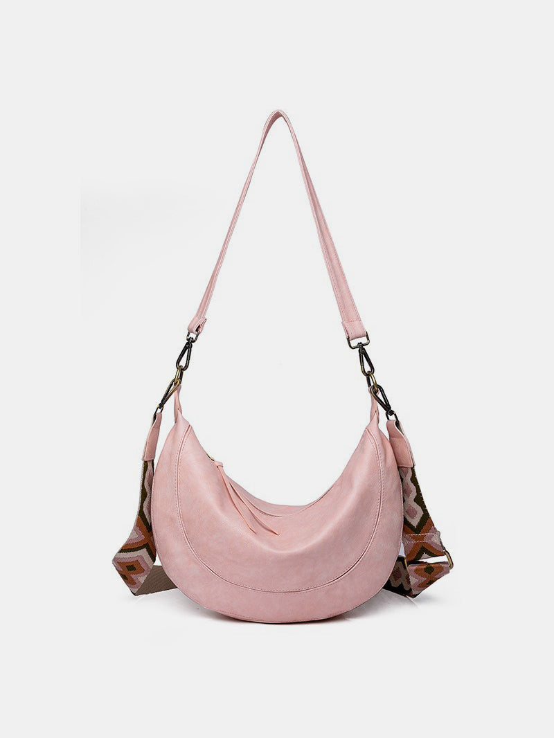 Large pink PU leather crossbody bag with a softly gathered crescent silhouette, long removable strap, zip-top construction, and metal clip hardware.