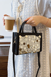 A model holds a small black PU leather handbag with a structured rectangular silhouette, rounded top handles, long shoulder strap, and sequin-covered front.