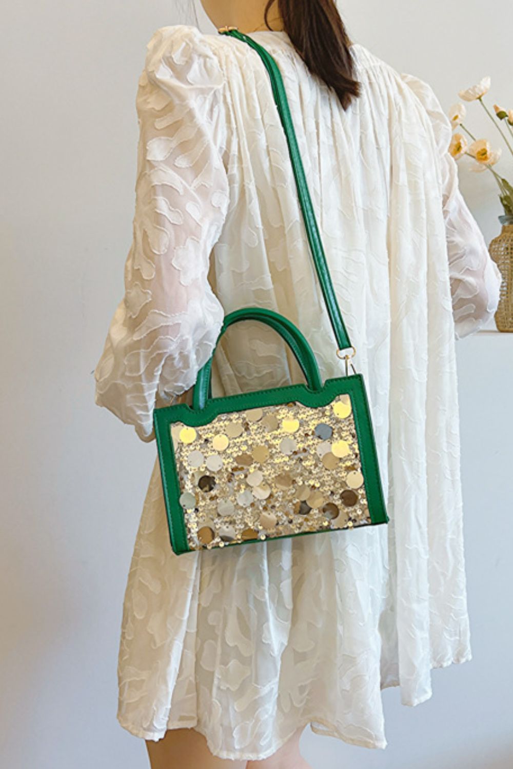 Model carries a small green PU leather handbag with a structured rectangular silhouette, rounded top handles, long shoulder strap, and shimmering sequin-covered front.