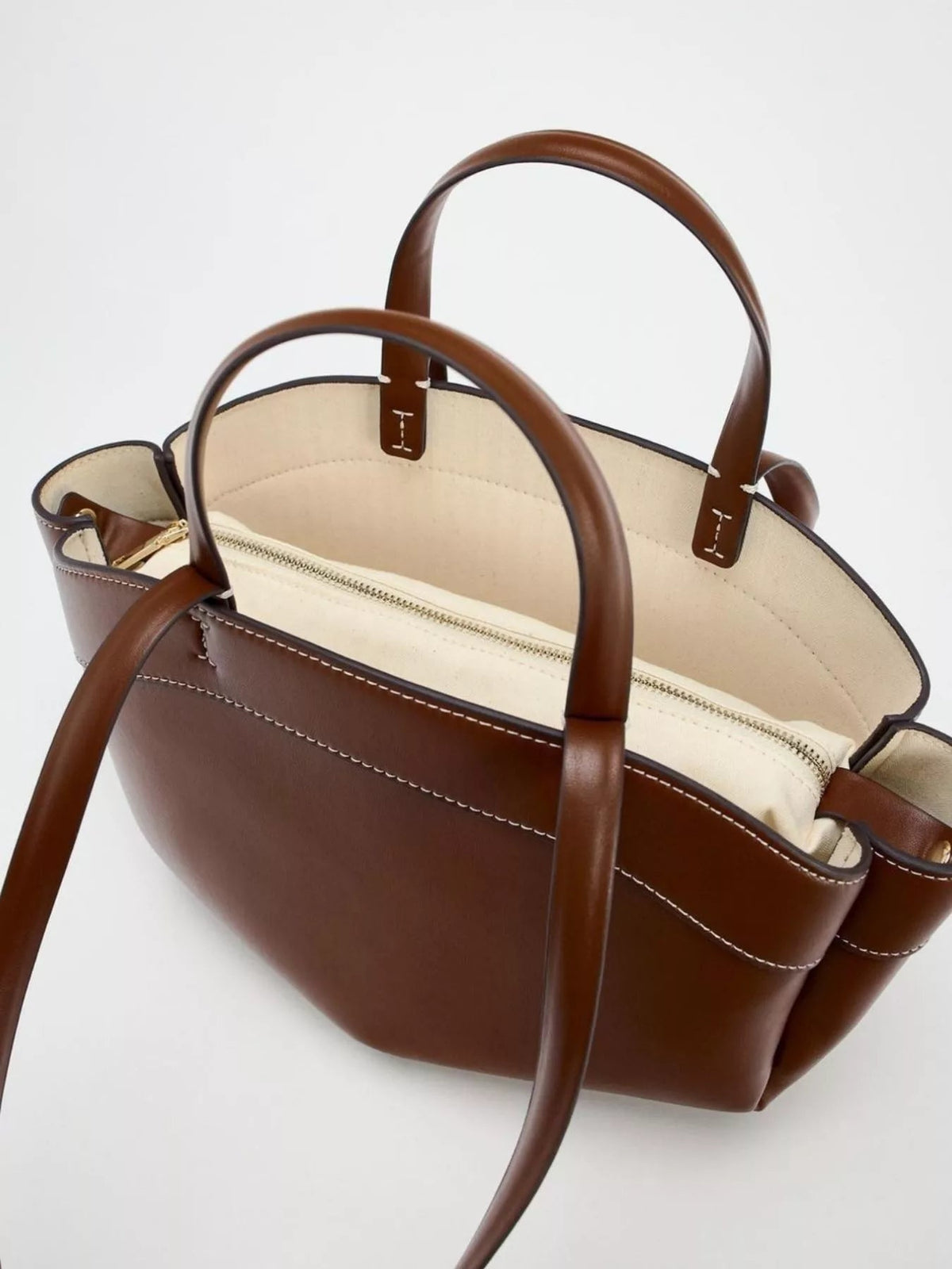 Large brown PU leather tote bag with double handles, contrasting cream interior, structured silhouette, white topstitching, and a central zippered compartment.
