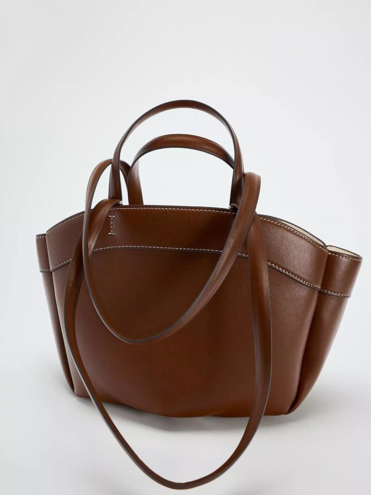 Large brown PU leather tote bag with structured silhouette, double top handles, long shoulder straps, and contrasting white stitching along the edges.