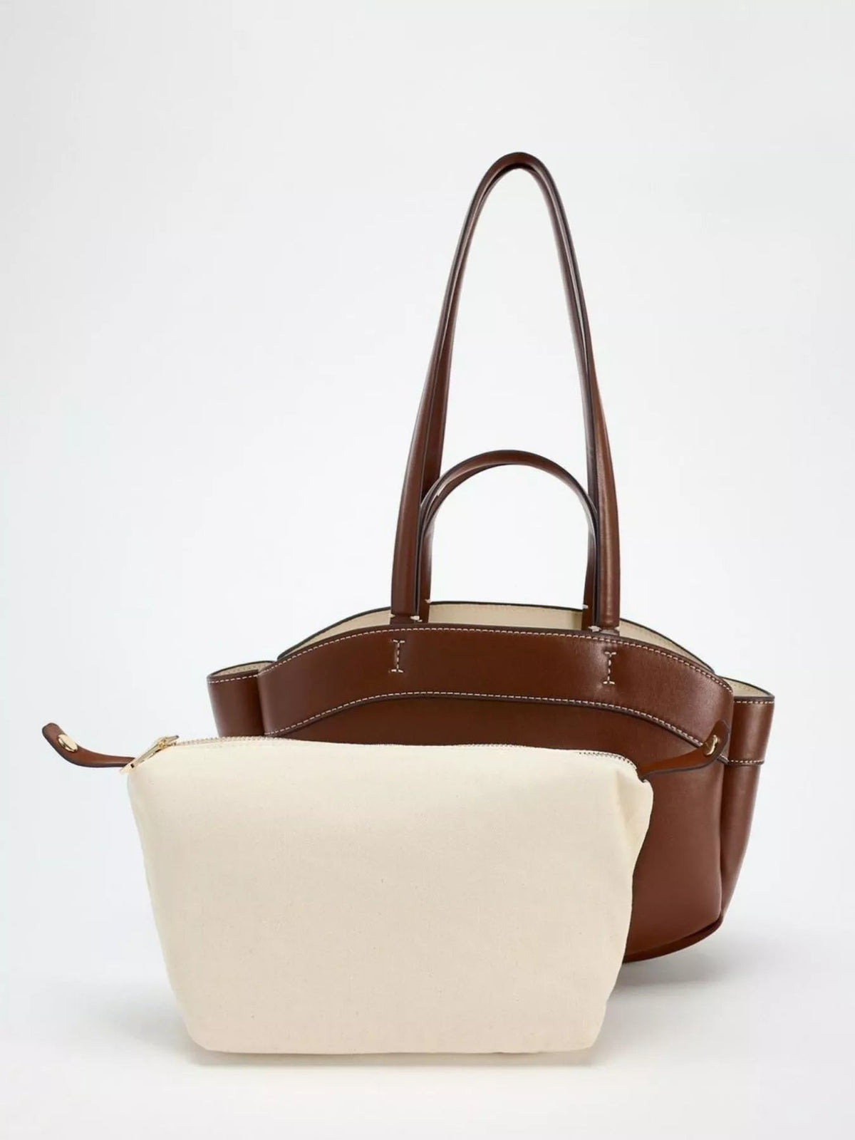 Large brown PU leather tote bag with a structured silhouette, tall double handles, contrast cream zip pouch, curved top edge, and visible stitching.