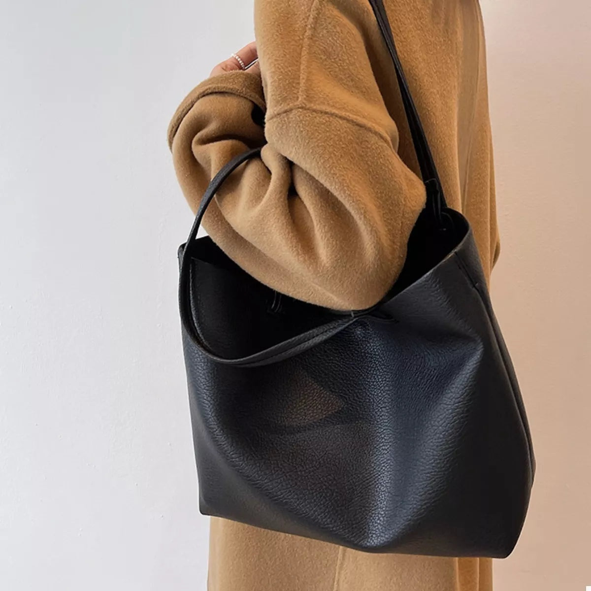 A model carries a large black PU leather tote bag over the shoulder, featuring a soft structured silhouette, open top, and long rounded handles.