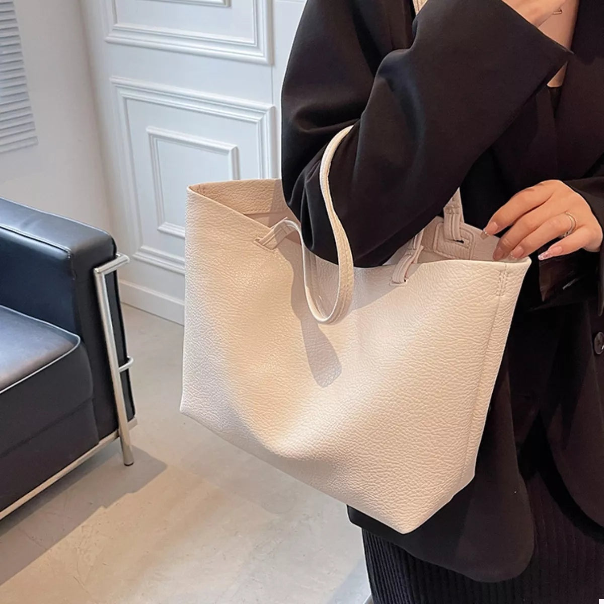 A model holds a large cream PU leather tote bag with a spacious open silhouette, pebbled texture, sturdy top handles, and long shoulder straps.