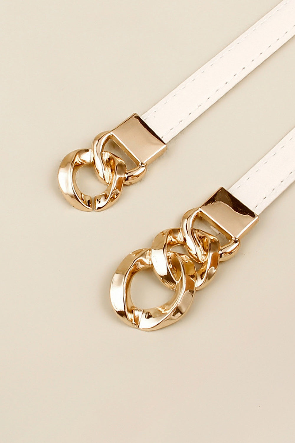 White PU skinny belt with stitched edges and polished gold-tone zinc alloy buckles featuring sculptural interlocking chain-link details.