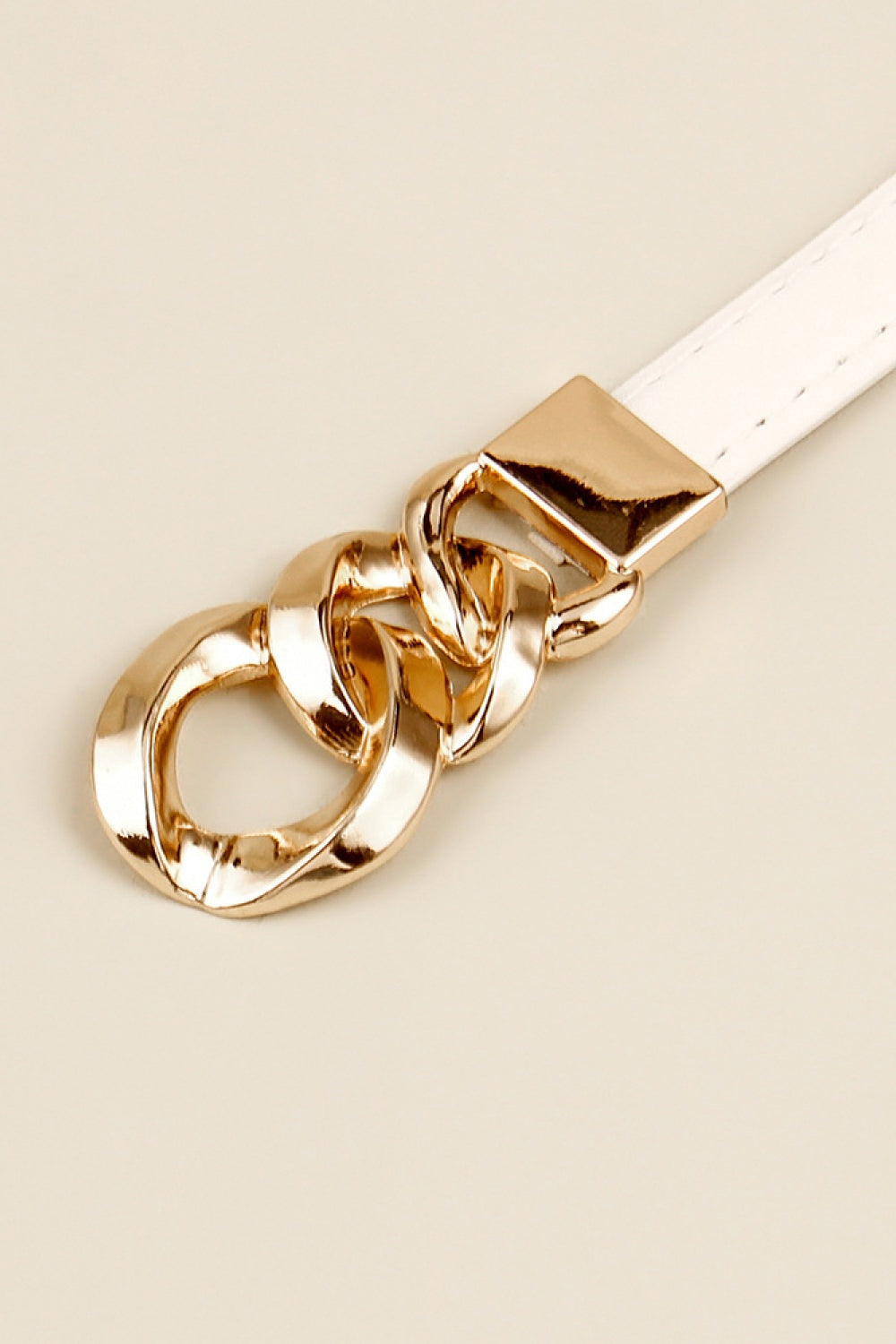 Close-up of a white PU skinny belt featuring a polished gold-tone zinc alloy buckle and sculptural chain-link detail.