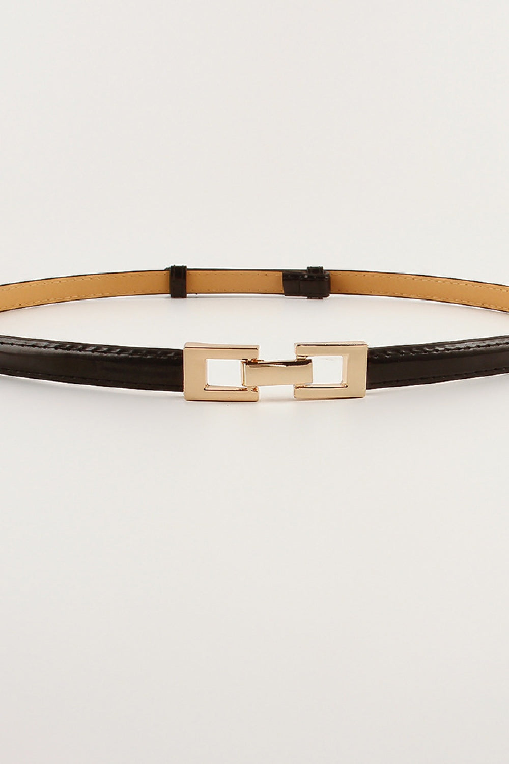 Black PU skinny belt with a polished geometric gold-tone buckle, shown flat to highlight its slim silhouette, stitched edges, and tan reverse.