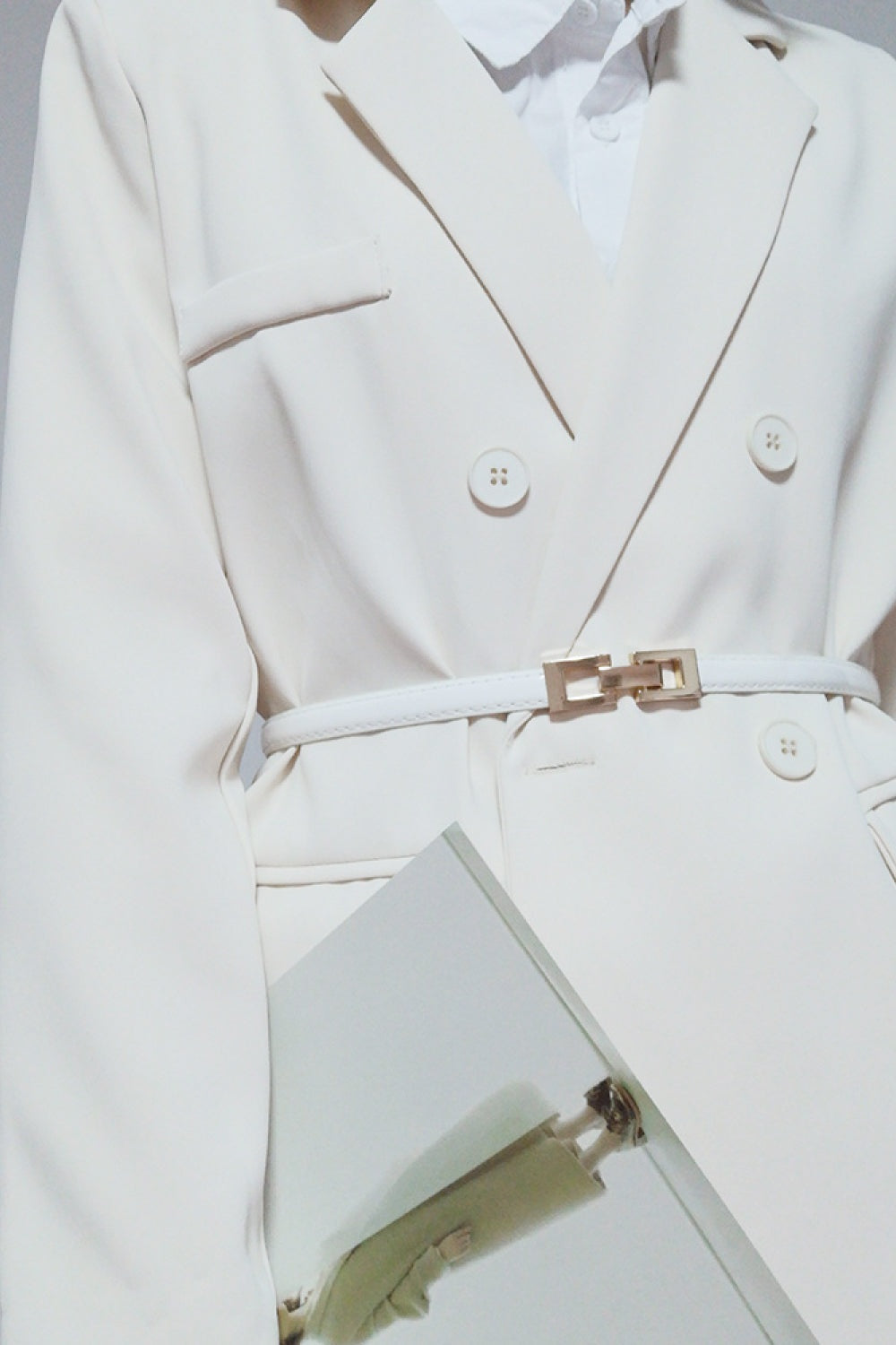 A model wears a white PU skinny belt with a polished geometric buckle, cinching the waist of a tailored white blazer and trousers.