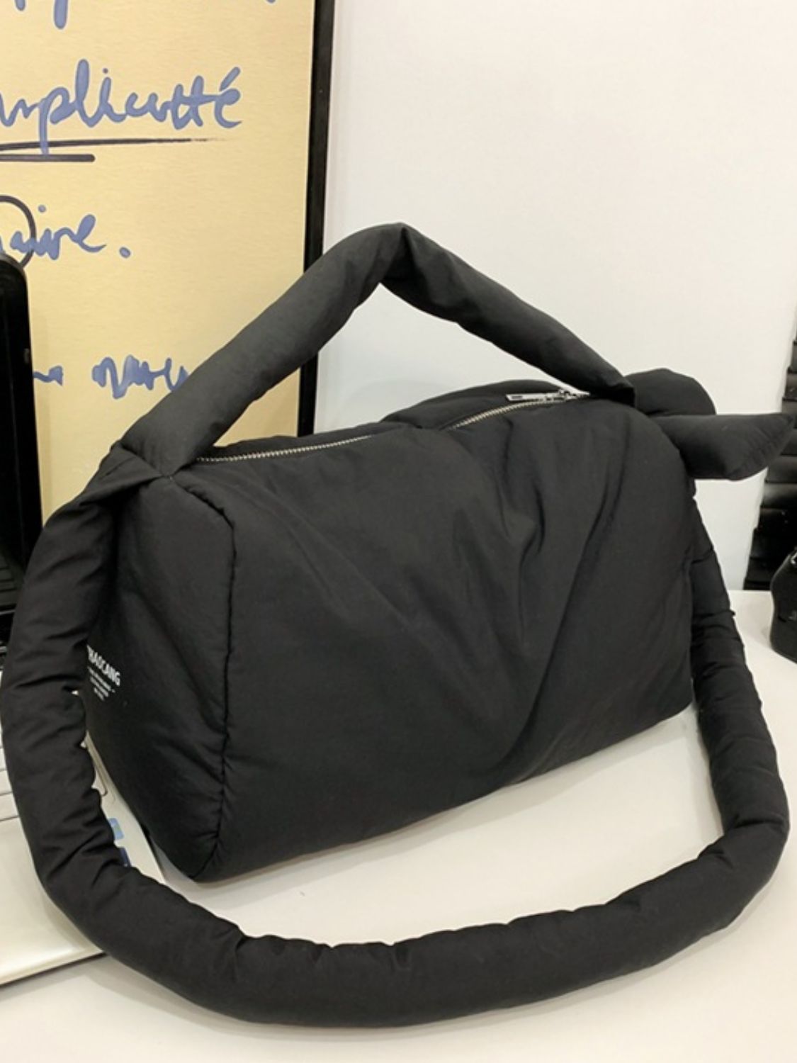 Black puffy nylon medium crossbody bag with a softly rounded padded silhouette, short top handle, long cushioned strap, and zip-top closure.