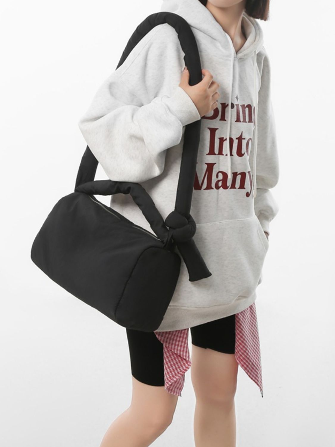A model carries a black puffy nylon medium crossbody bag at her side, showing its softly rounded silhouette, padded construction, and long strap.
