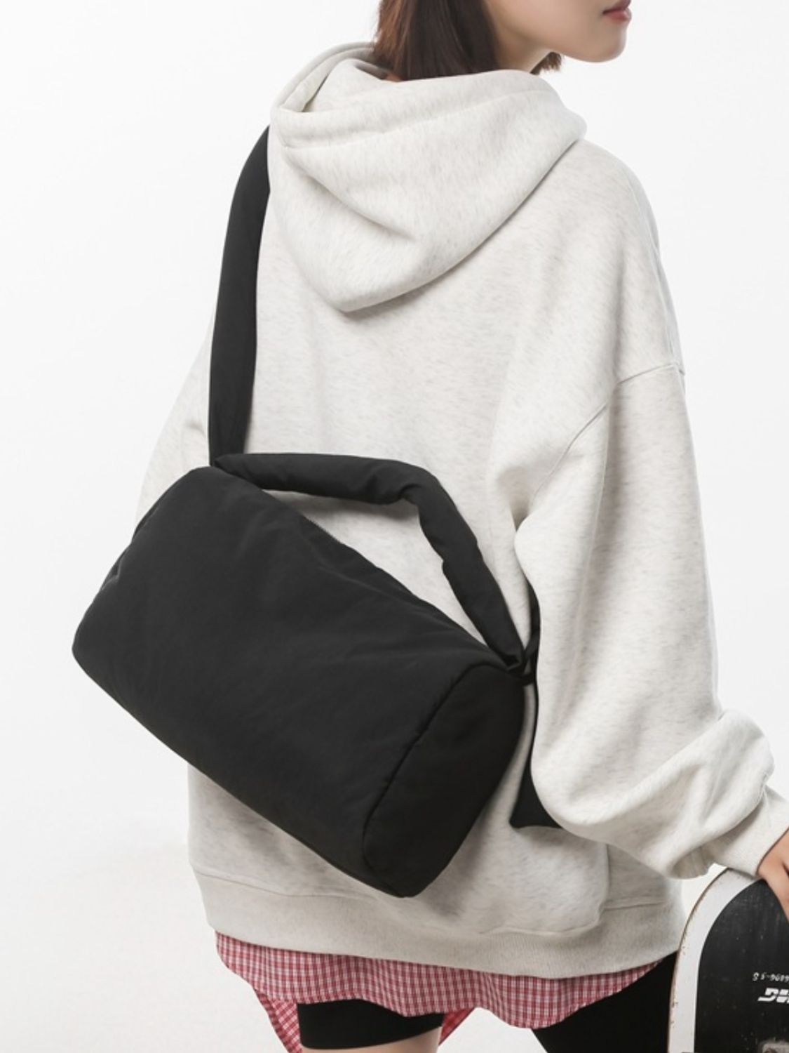 Model in a light gray hoodie wears a black puffy nylon medium crossbody bag with a softly rounded silhouette, padded construction, and wide strap.