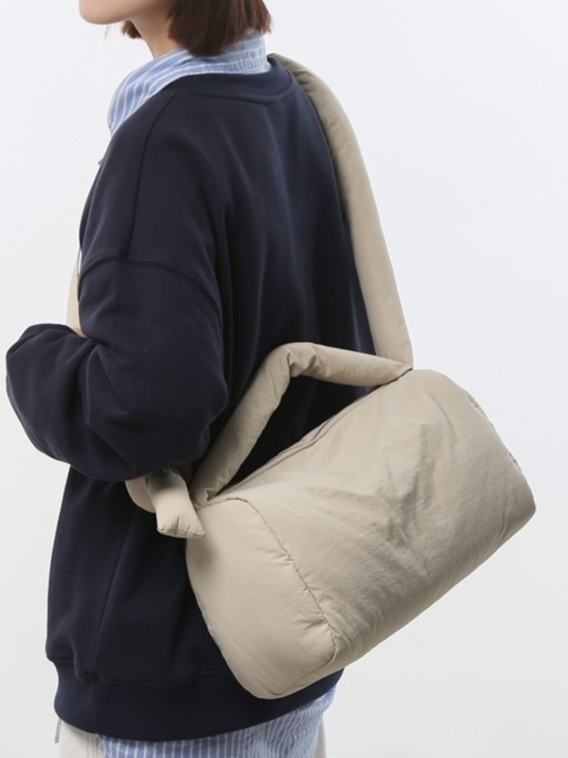 A model carries a cream puffy nylon medium crossbody bag over one shoulder, showcasing its rounded padded silhouette, softly gathered edges, and relaxed construction.
