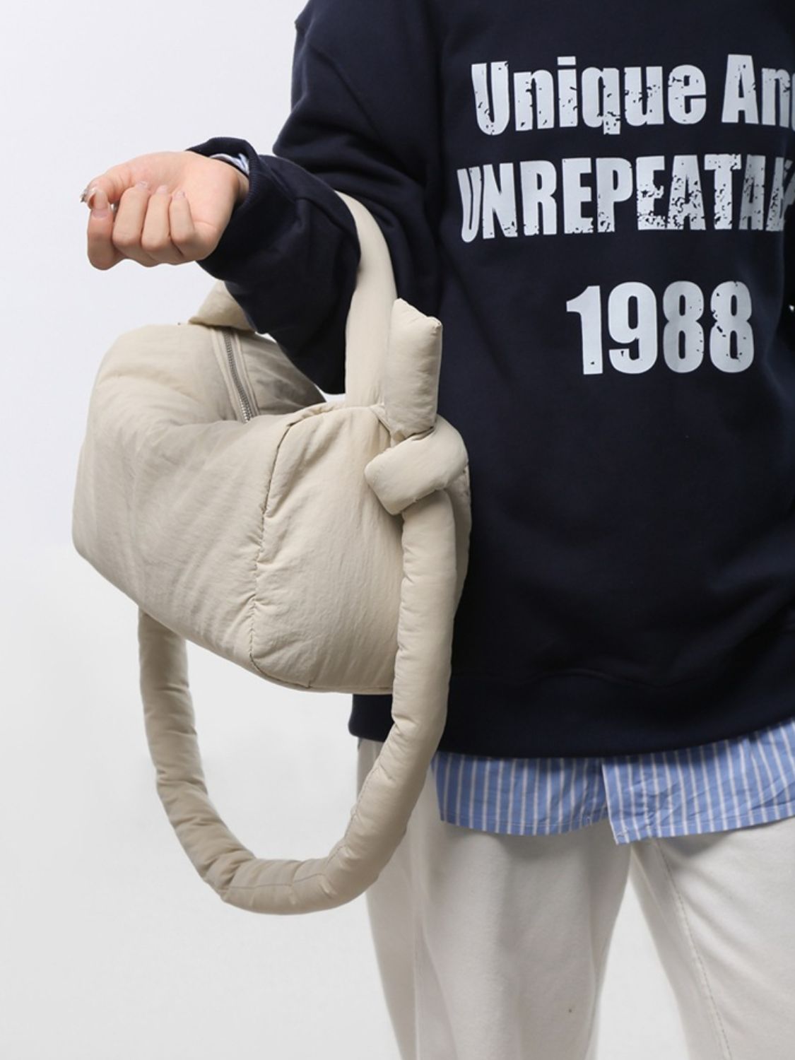 Model holds a cream puffy nylon medium crossbody bag by its padded top handle, showing its softly rounded silhouette and gathered construction.