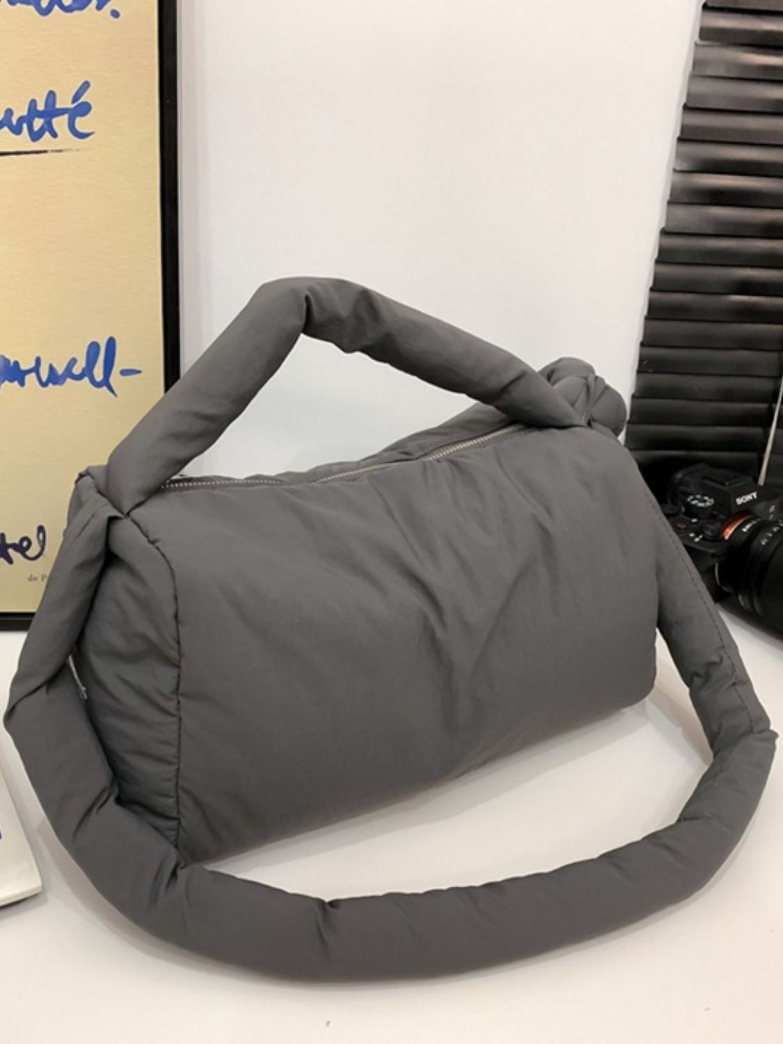 Gray puffy nylon medium crossbody bag with a softly rounded, padded silhouette, zip-top opening, short top handle, and long padded strap.