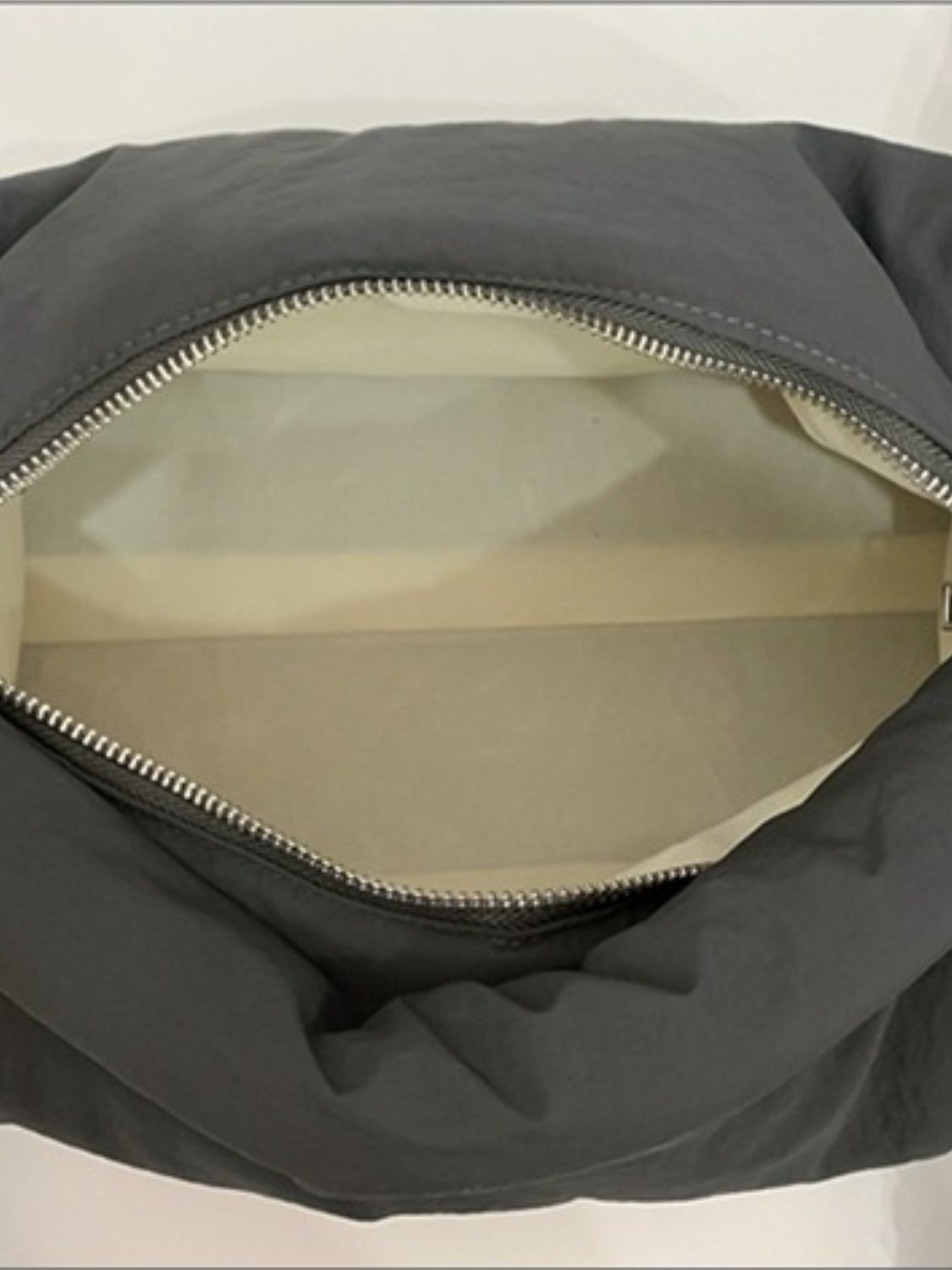 An open black puffy nylon crossbody bag reveals its spacious light-colored interior and curved zip-top opening with softly gathered construction.