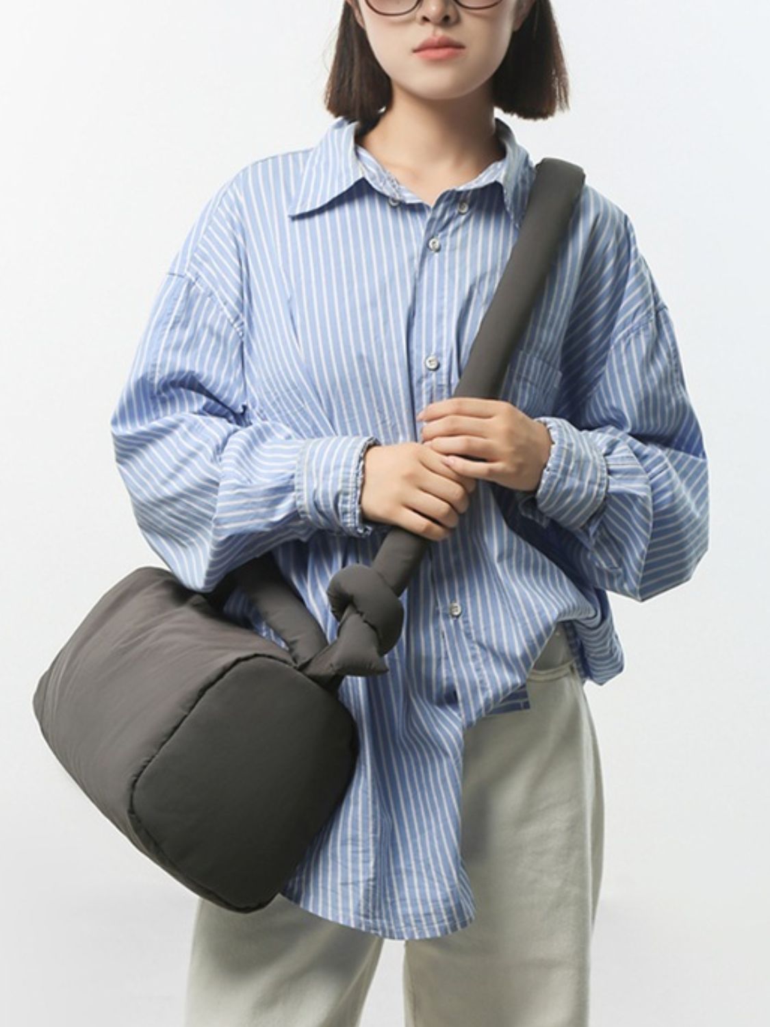 A model holds a dark gray puffy nylon medium crossbody bag with a softly rounded silhouette, padded construction, and long cushioned strap worn across the body.