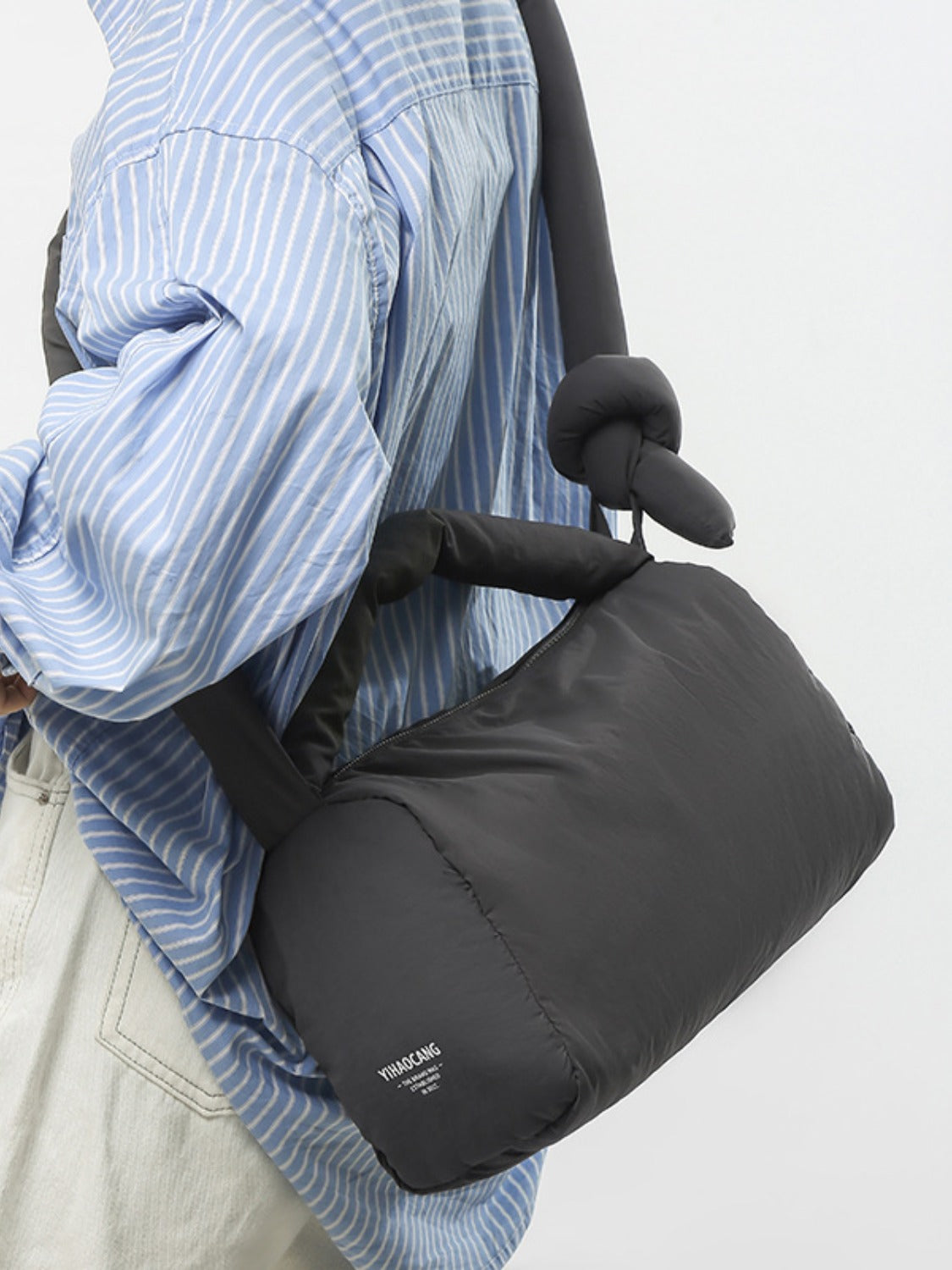 A model carries a black puffy nylon medium crossbody bag at her side, featuring a rounded silhouette, padded construction, and a zip-top opening.