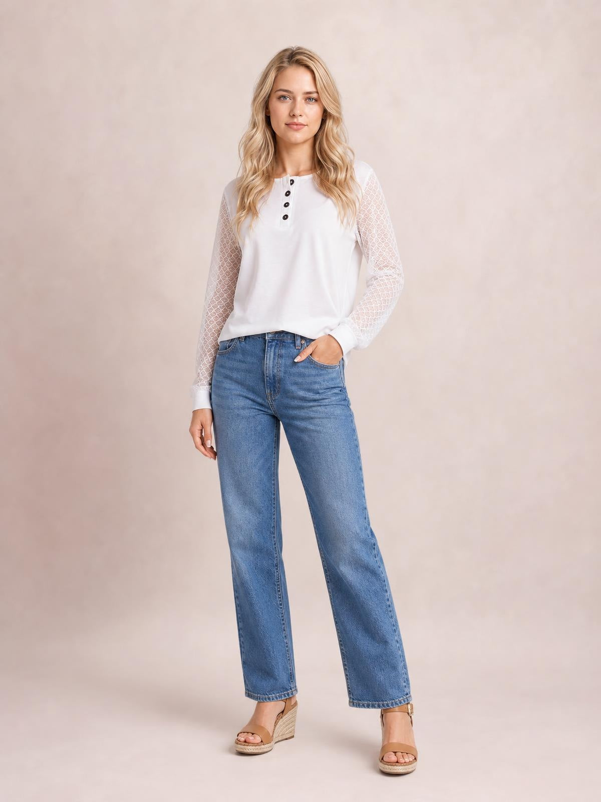 Model wearing a white quarter-button round-neck long-sleeve blouse with lace-detail semi-sheer sleeves and a relaxed silhouette, posing with one hand in her jeans pocket.