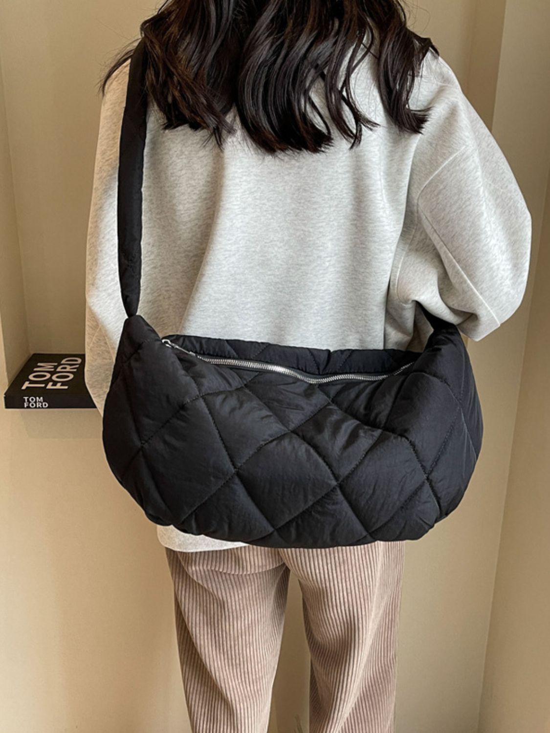 A model wears a large black quilted crossbody bag with a softly structured crescent silhouette, plush diamond stitching, and a zip-top opening.