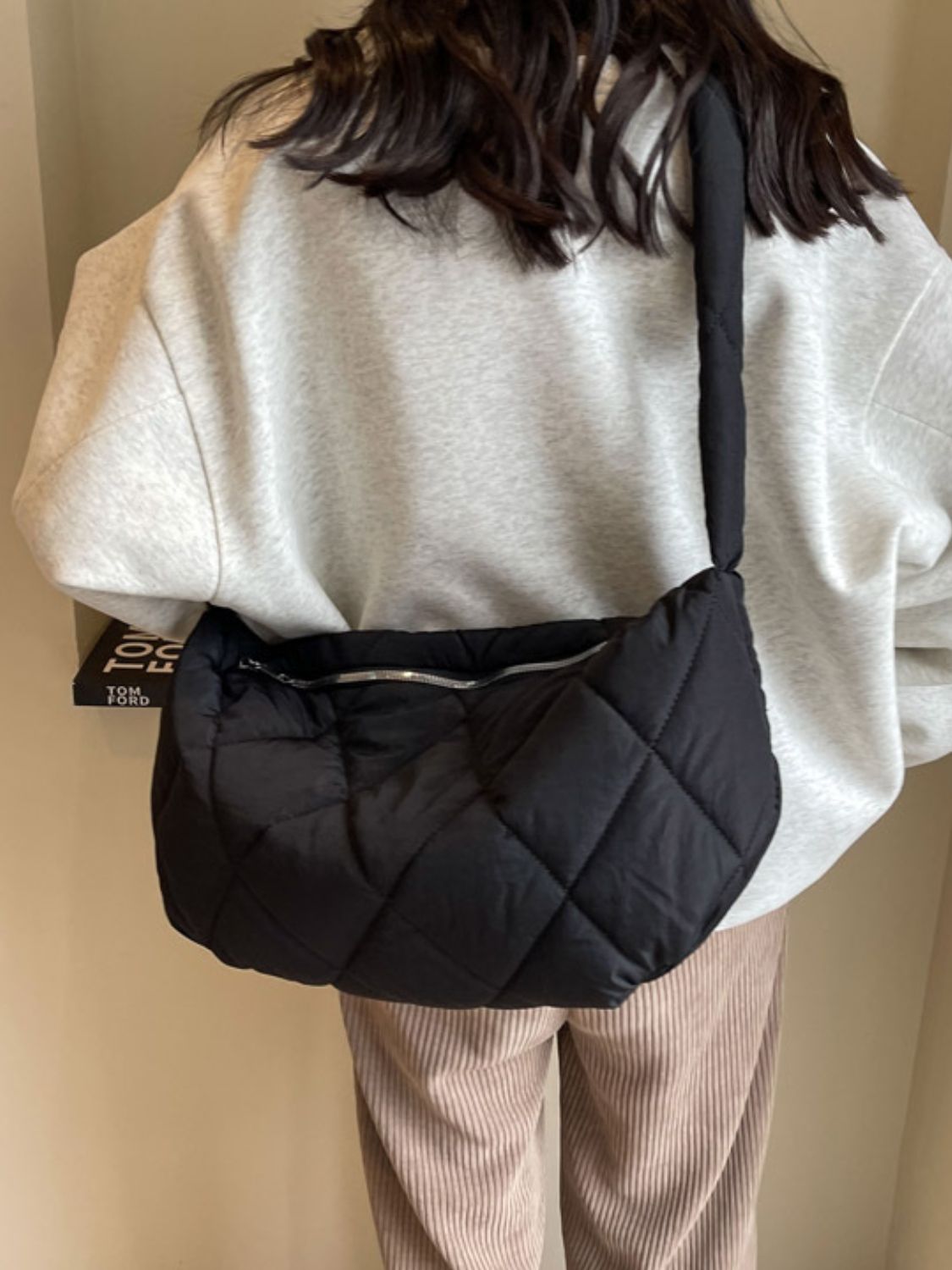 Model wears a large black quilted crossbody bag with a softly structured crescent silhouette, plush diamond stitching, long strap, and zip-top opening.