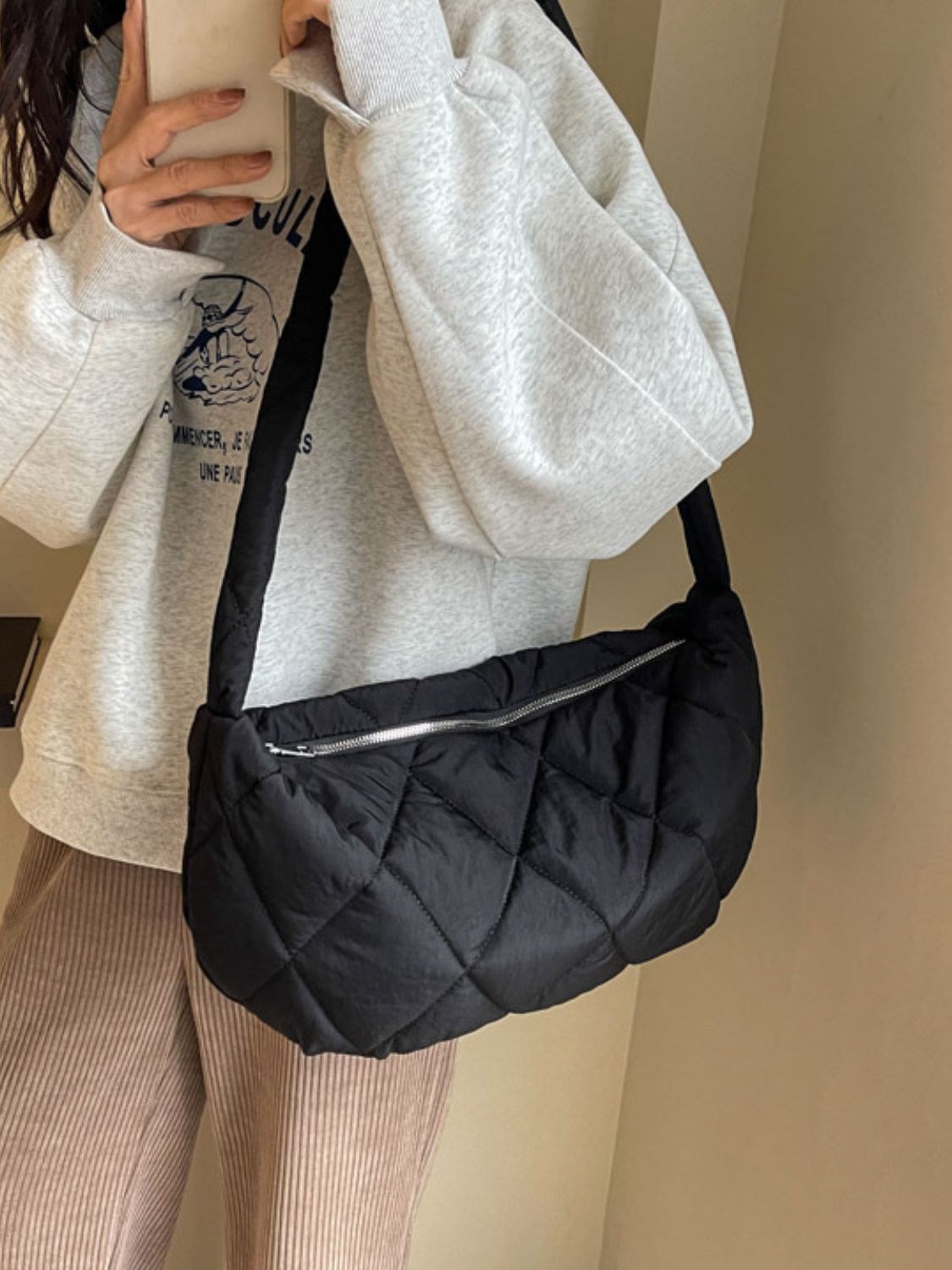 Model wears a large black quilted crossbody bag with a softly rounded crescent silhouette, plush diamond stitching, long strap, and silver zip-top closure.