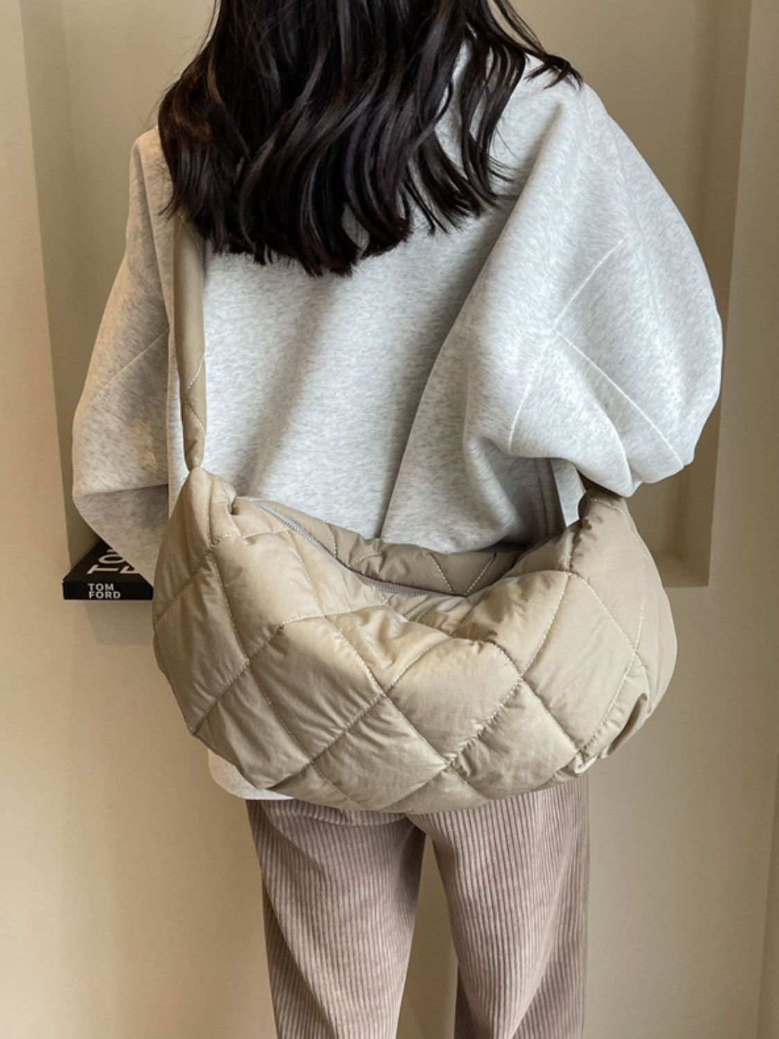 Model wearing a large beige quilted crossbody bag with a softly structured crescent silhouette, plush diamond stitching, and a long strap across the torso.