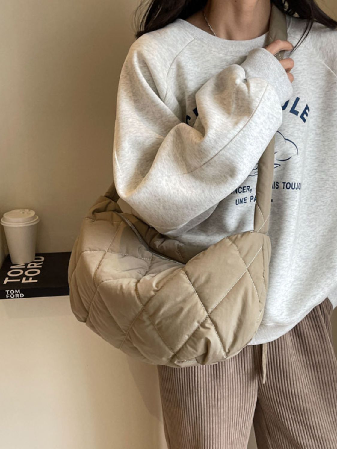 Model wearing a large beige quilted crossbody bag with a softly structured crescent silhouette, plush diamond stitching, and a long strap across the torso.