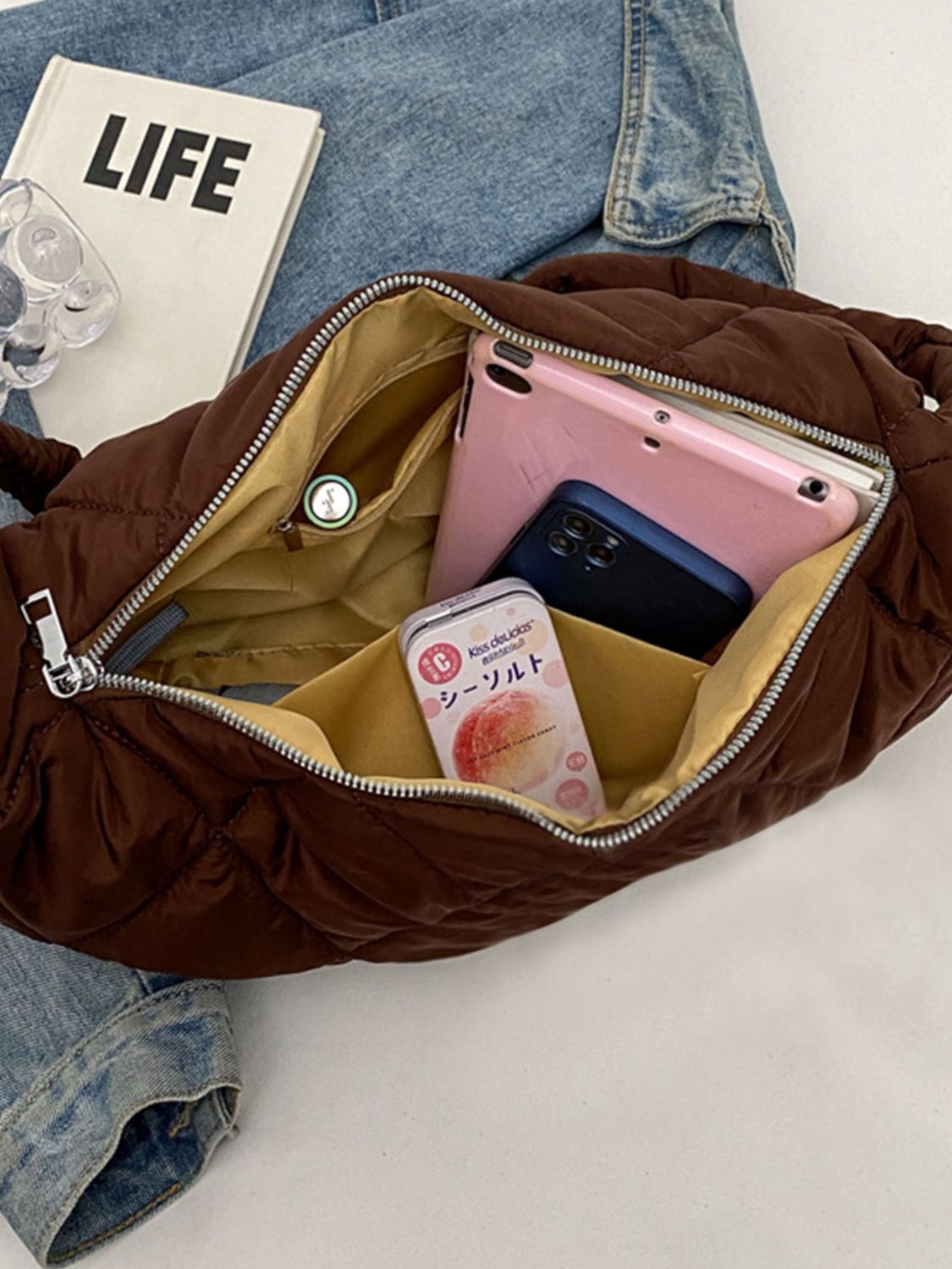 Large brown quilted crossbody bag shown open on denim, featuring a softly rounded silhouette, roomy interior, and secure zip-top opening.