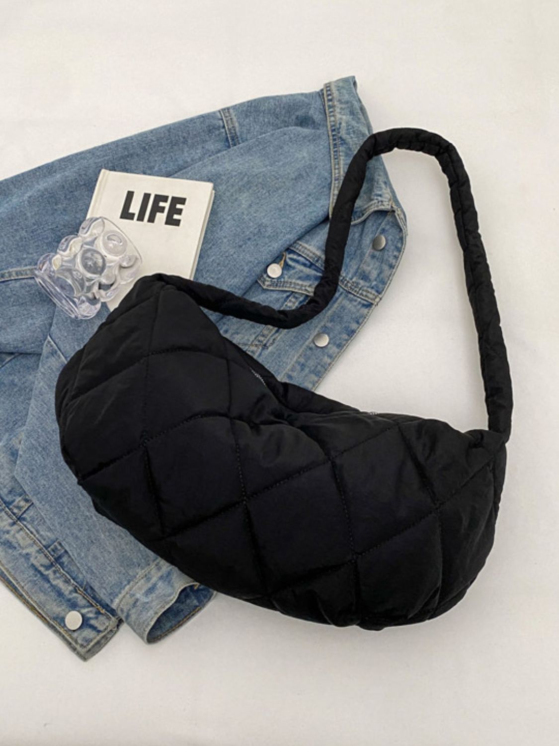 Black quilted crossbody bag with a softly structured crescent silhouette, plush volume, and a long padded strap.