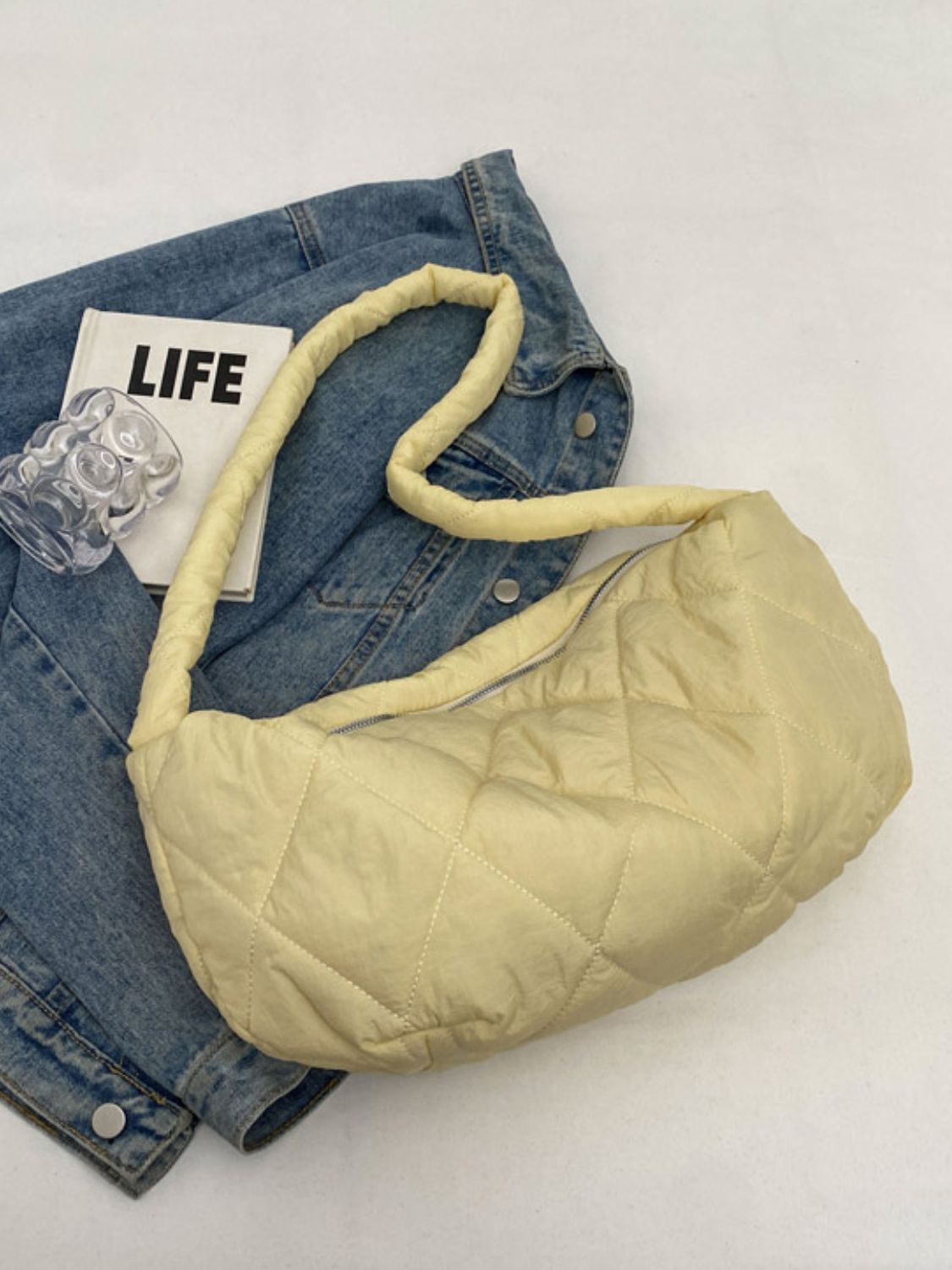 Large pale yellow quilted crossbody bag with a softly structured crescent silhouette, plush diamond stitching, long strap, and visible zip-top closure.