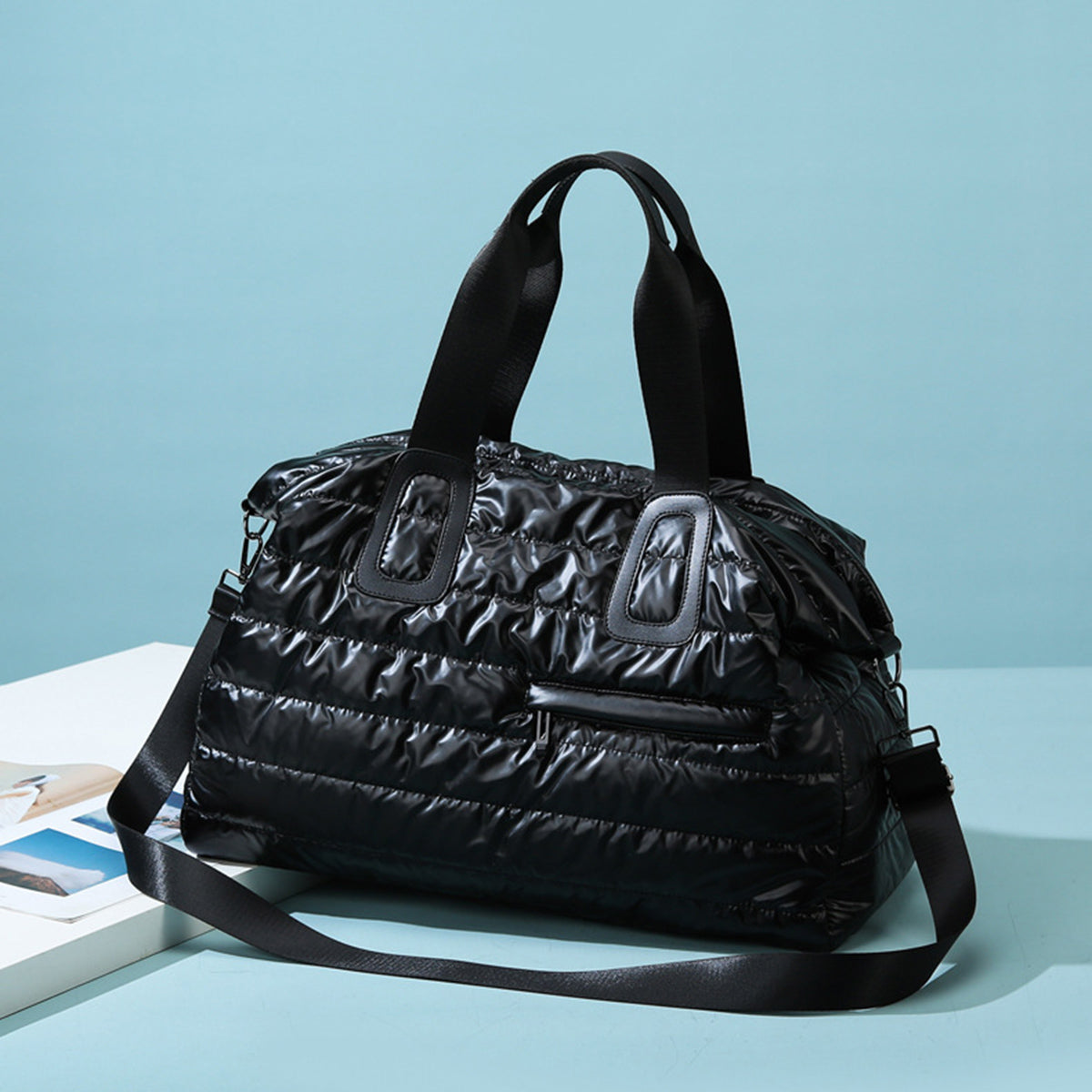 Black quilted nylon oversize travel bag with padded horizontal quilting, sturdy top handles, a long shoulder strap, and a front zip pocket.