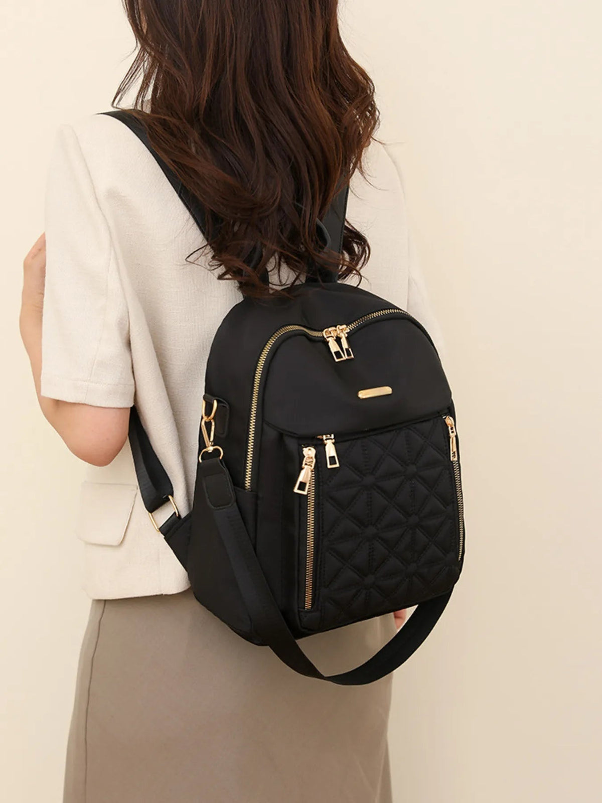 A model wears a medium black quilted Oxford cloth backpack with a rounded silhouette, gold-tone zippers, front zip pocket, and wide shoulder straps.