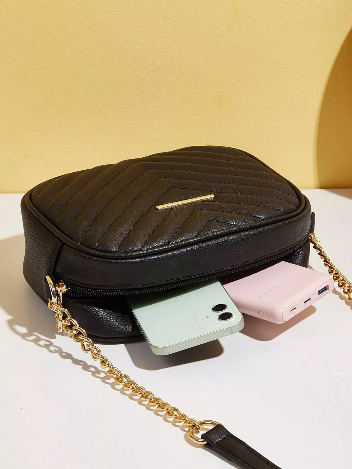 Black mini quilted PU leather crossbody bag with a structured rounded silhouette, gold chain strap, zippered compartment, and polished bar accent.