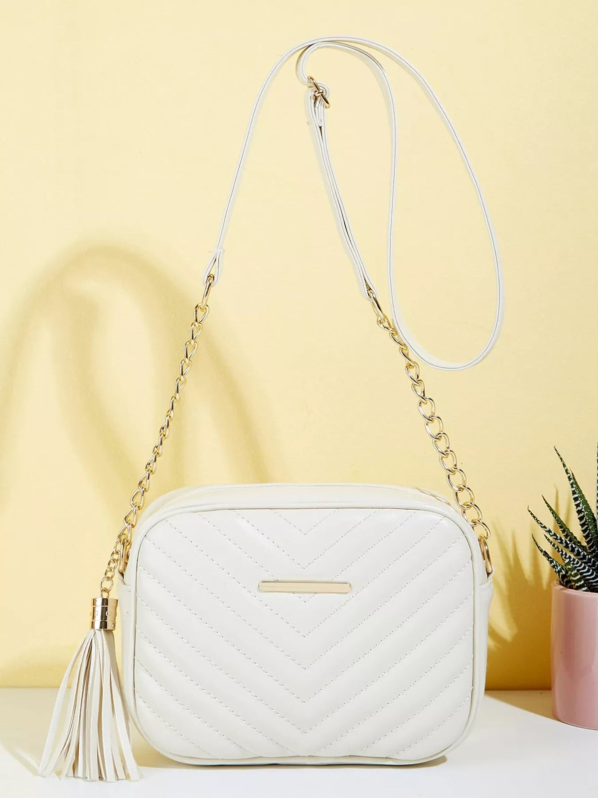 White mini PU leather crossbody bag with chevron quilting, rounded rectangular shape, gold chain and strap, and a long matching tassel.