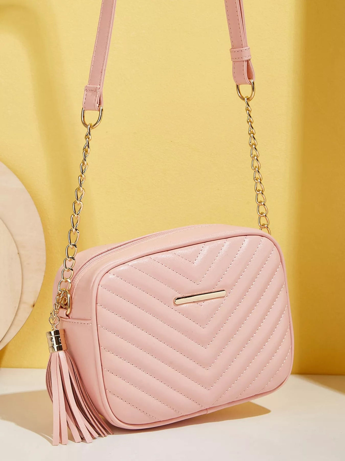 Pink mini PU leather crossbody bag with chevron quilting, rounded rectangular silhouette, gold chain strap, zip closure, and a long tassel.